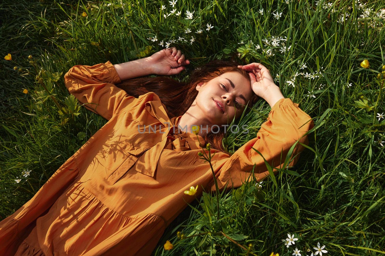 a woman, resting lying in the grass, in a long orange dress, with her eyes closed and a pleasant smile on her face, touching her face with her hand, and enjoying harmony with nature and recuperating by Vichizh