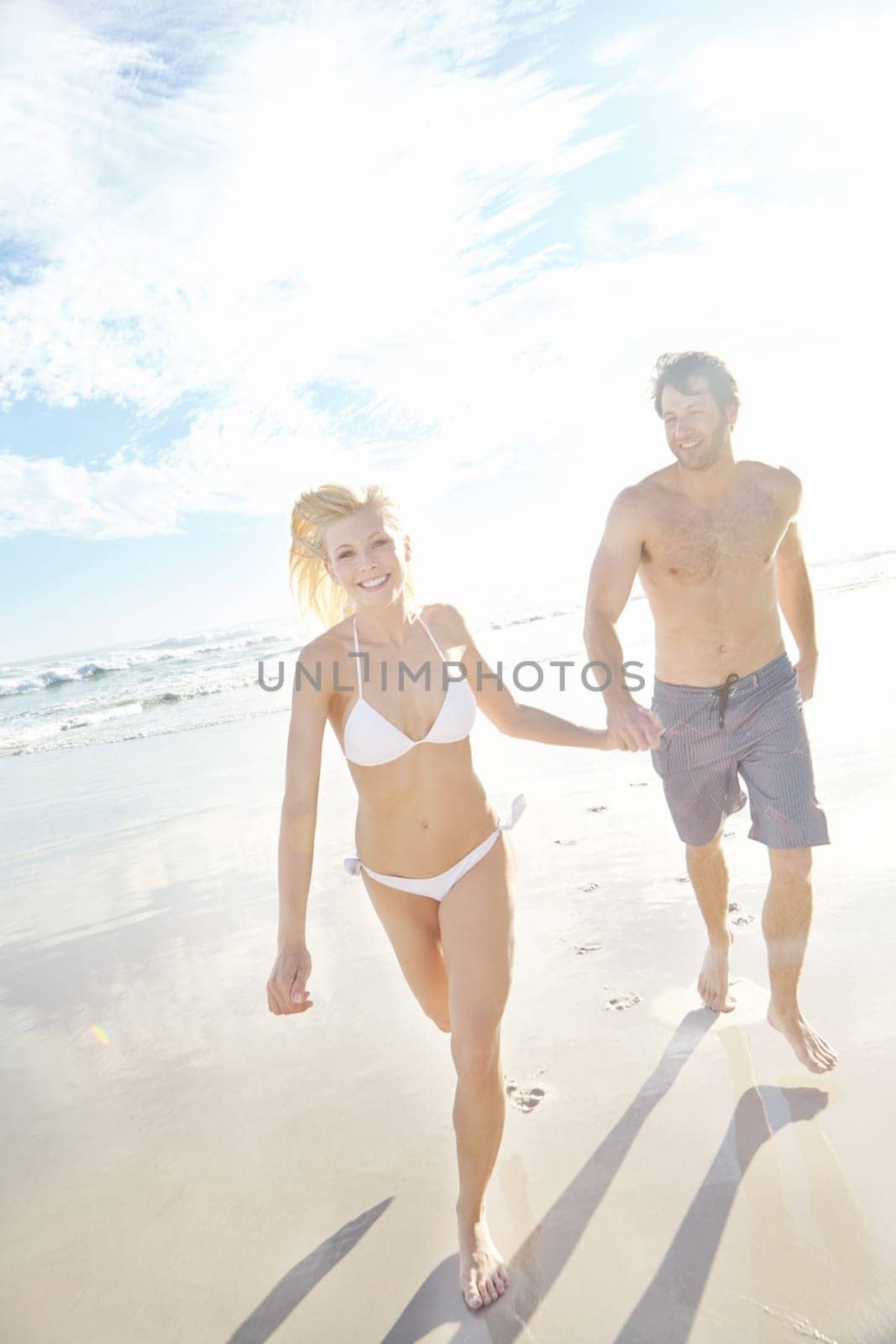 Beauty and the beach. a young couple running on a beach. by YuriArcurs