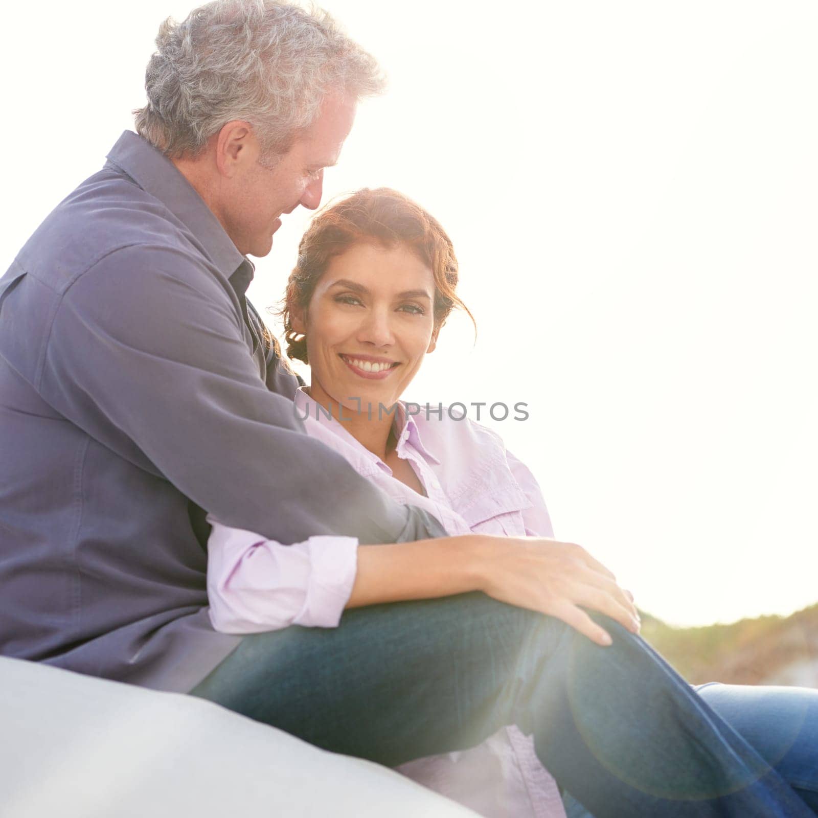 Their love is a special thing. A mature couple hugging one another while sitting on a sand dune. by YuriArcurs