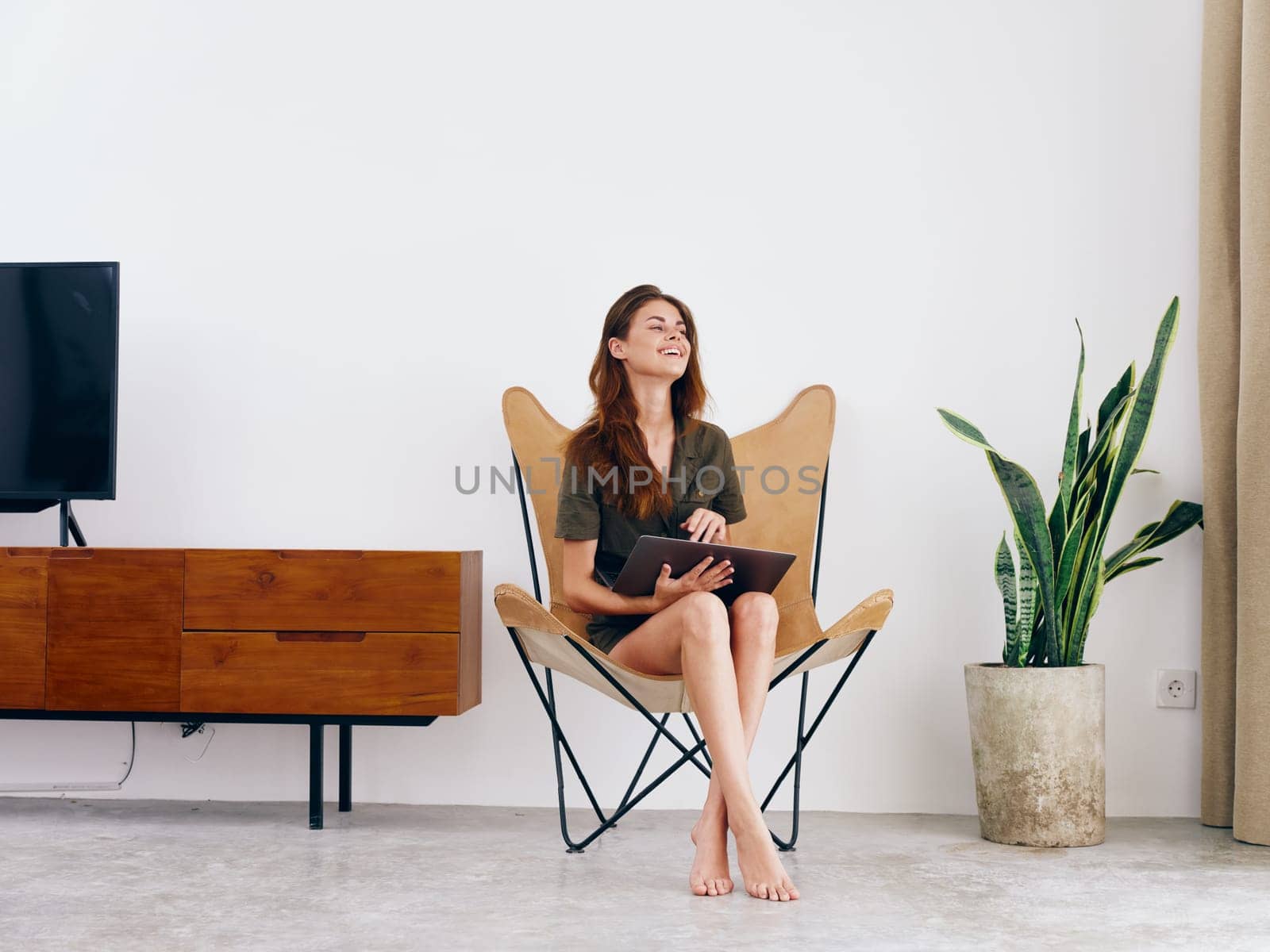 Woman student study sits on a chair with a laptop work at home smile, modern stylish interior Scandinavian lifestyle, copy space. by SHOTPRIME