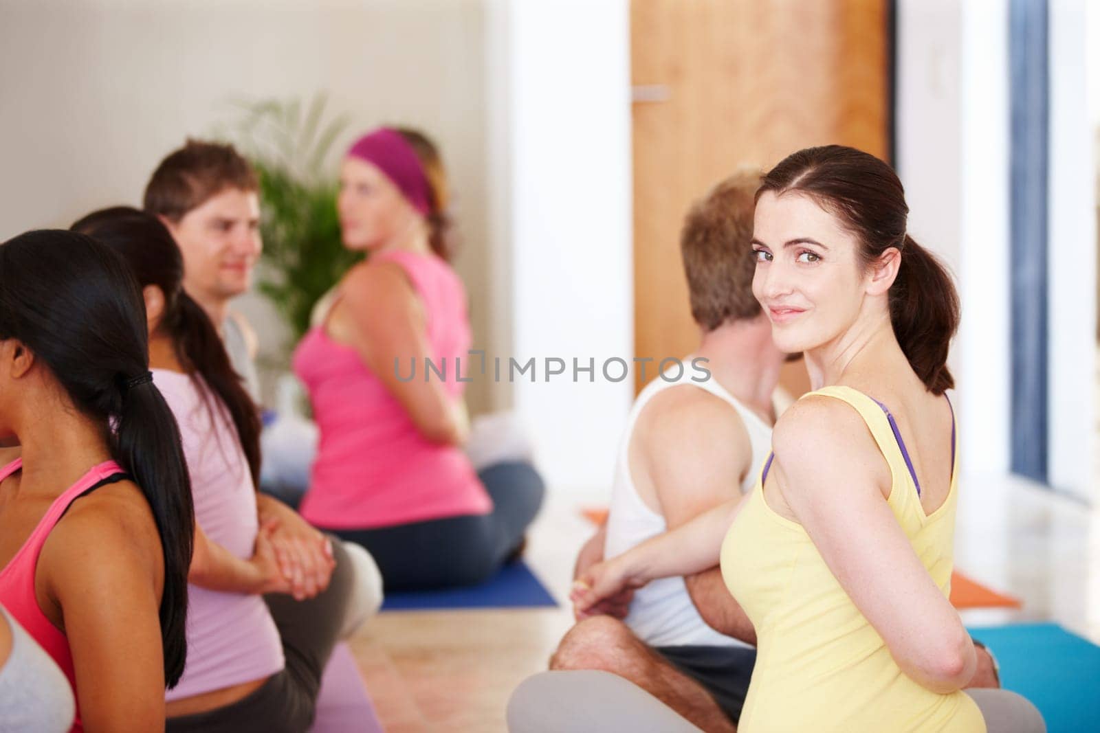 Enjoying a yoga class. Portrait of a happy woman sitting and doing stretches during a yoga class. by YuriArcurs