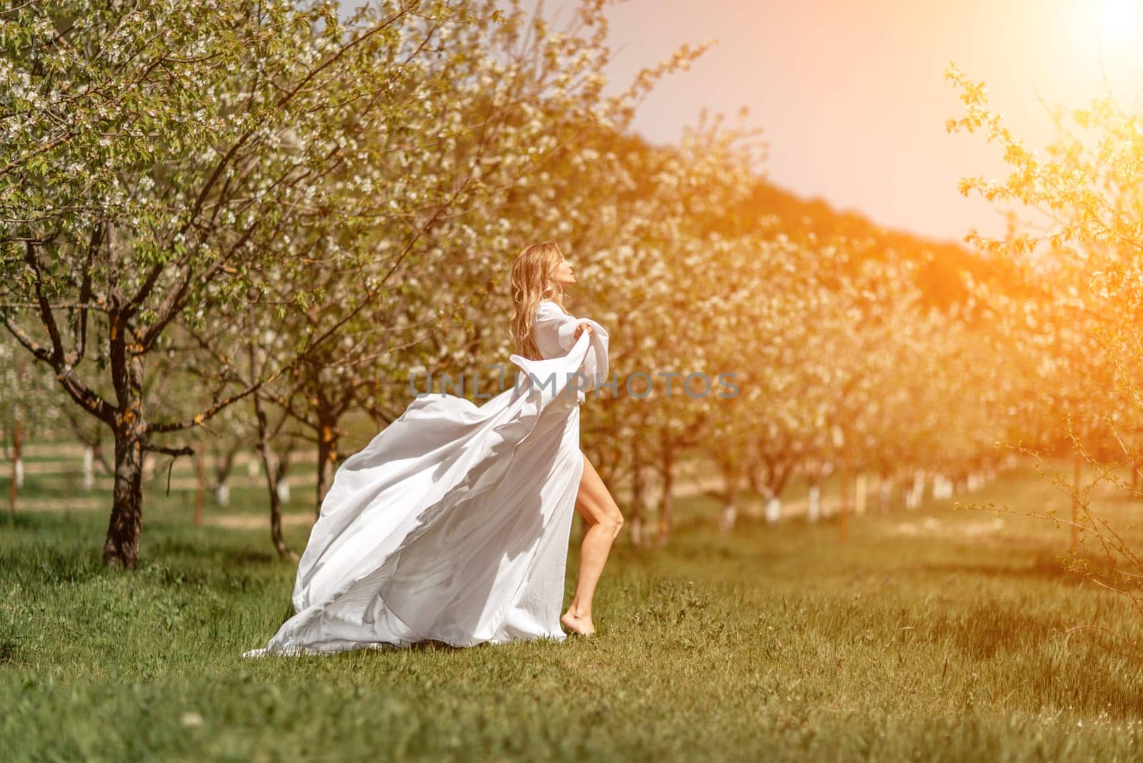 Woman white dress park. A woman in a white dress runs through a blossoming cherry orchard. The long dress flies to the sides, the bride runs rejoicing in life