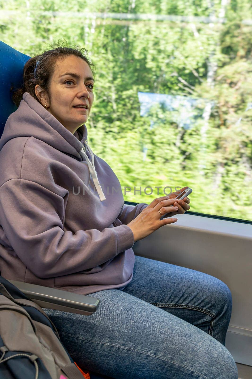 a pretty woman is riding on a commuter train, sitting at the window and flipping through the news feed in her smartphone. I'm going to work on a commuter train. A fun trip. Work while traveling on public transport. The concept of remote work, vertical photo, freelancer