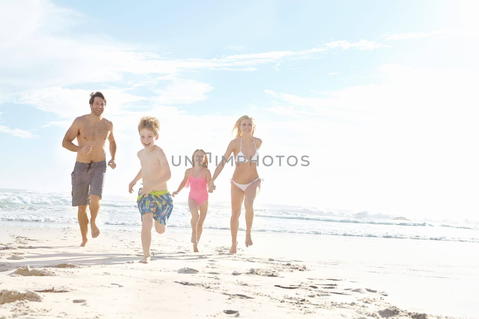 Family fun in the sun. a happy young family running on the beach together. by YuriArcurs