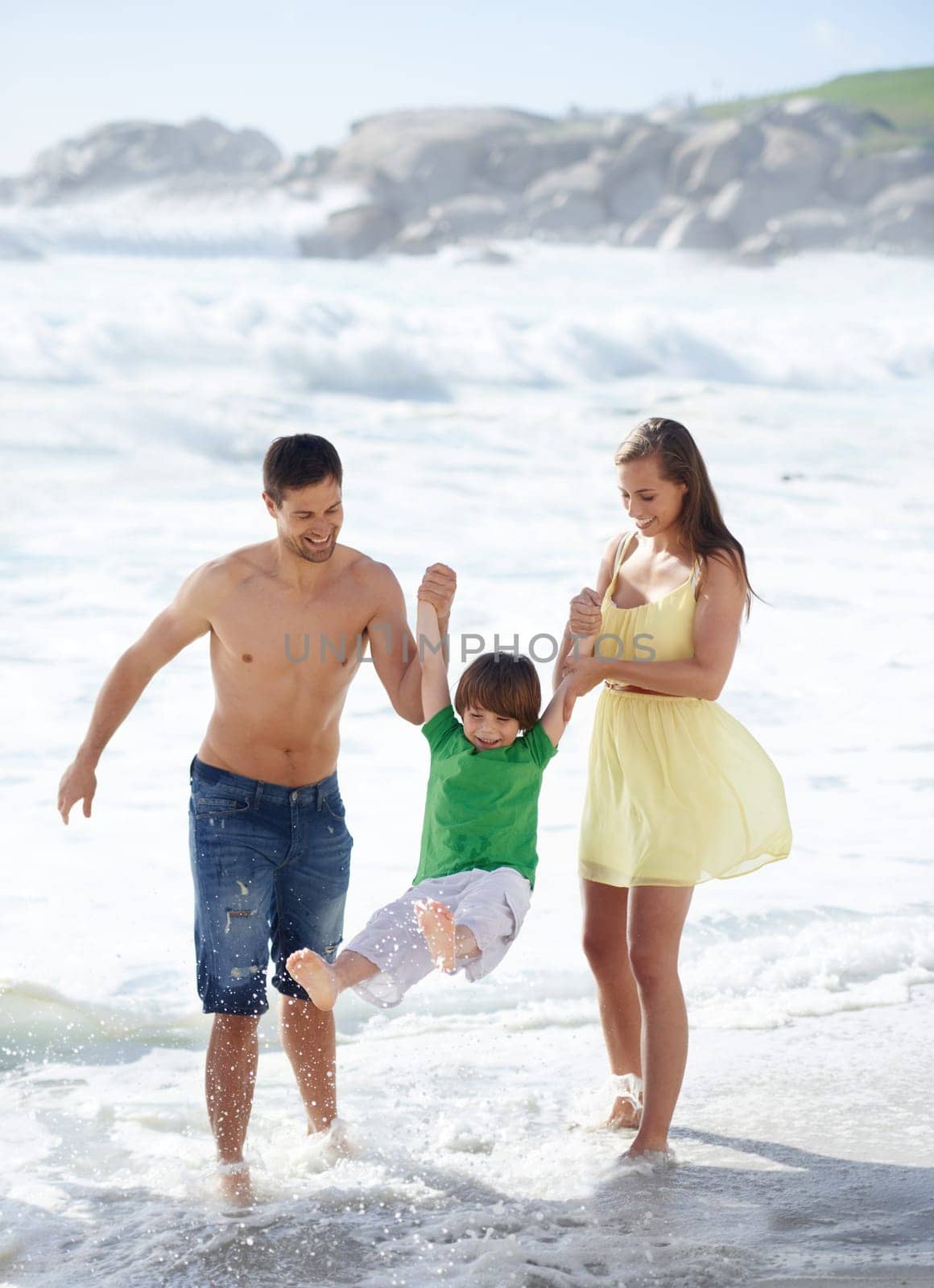 Family, summer and swinging child at beach for fun, travel or holiday with a smile in water. A man, woman and kid or son playing together on vacation at sea with waves, love and happiness outdoor.