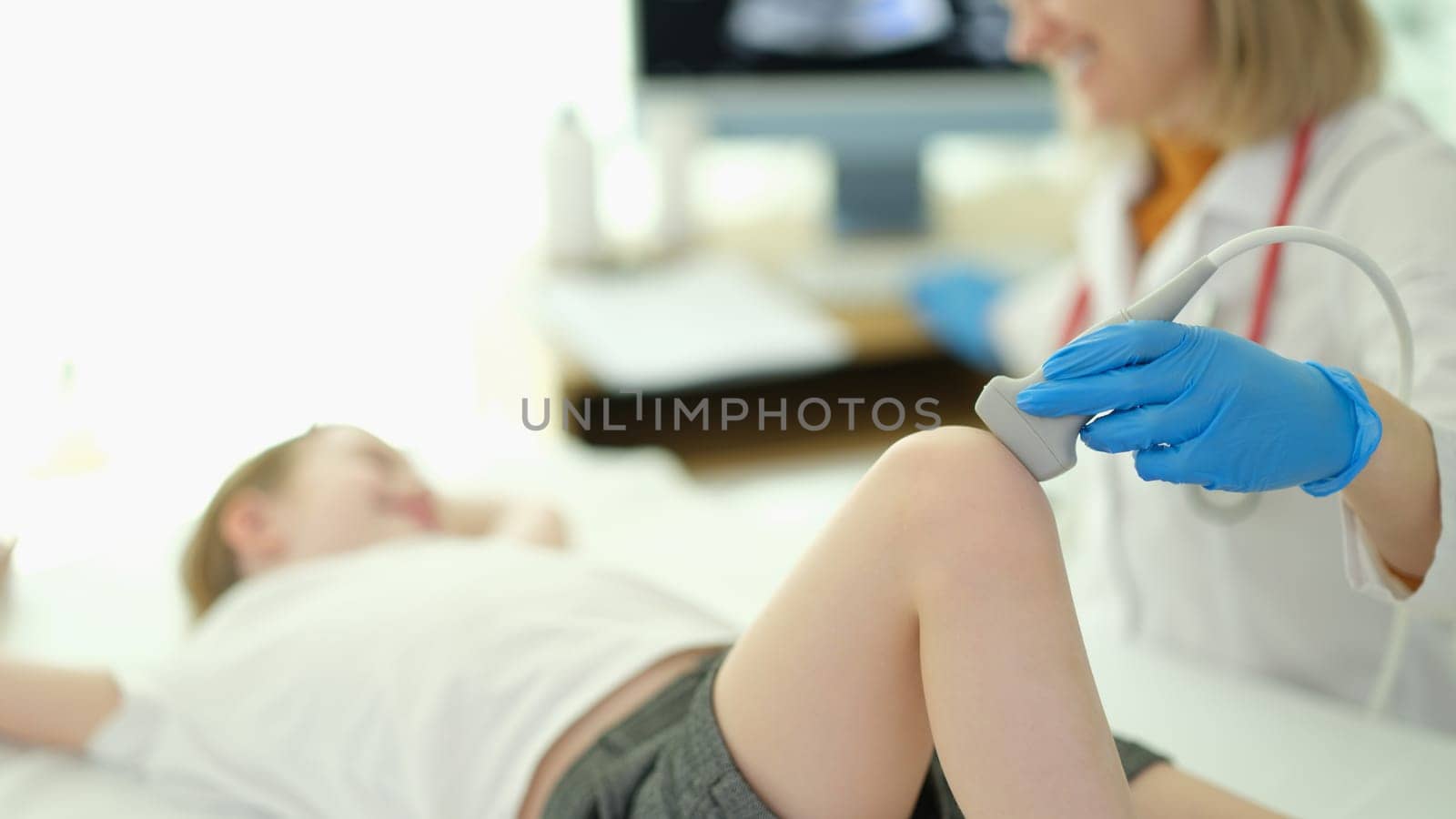 Doctor traumatologist making ultrasound examination of knee joint to child in clinic closeup. Diseases of bones and joints in children concept