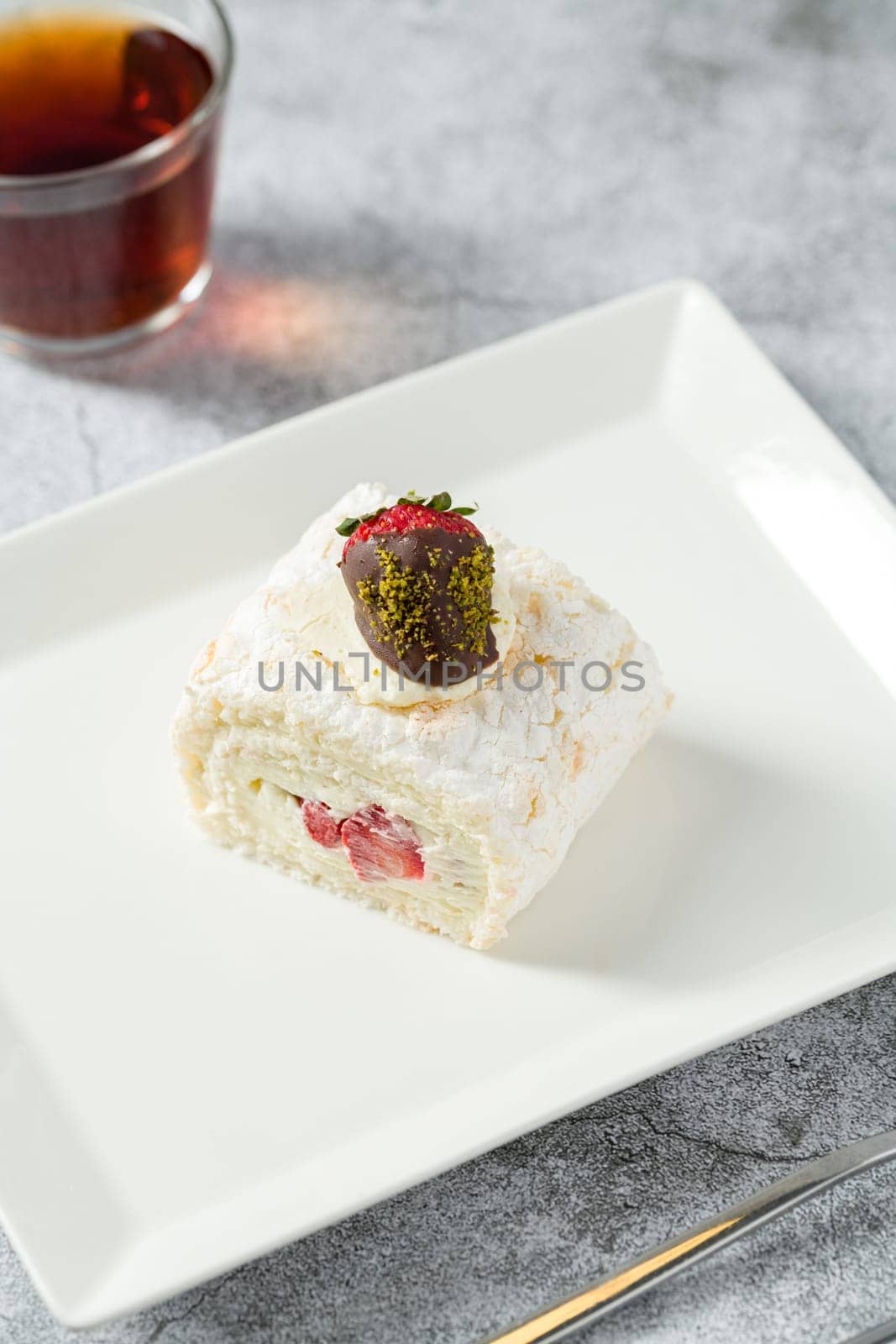 Strawberry roll cake with tea next to it on stone table by Sonat