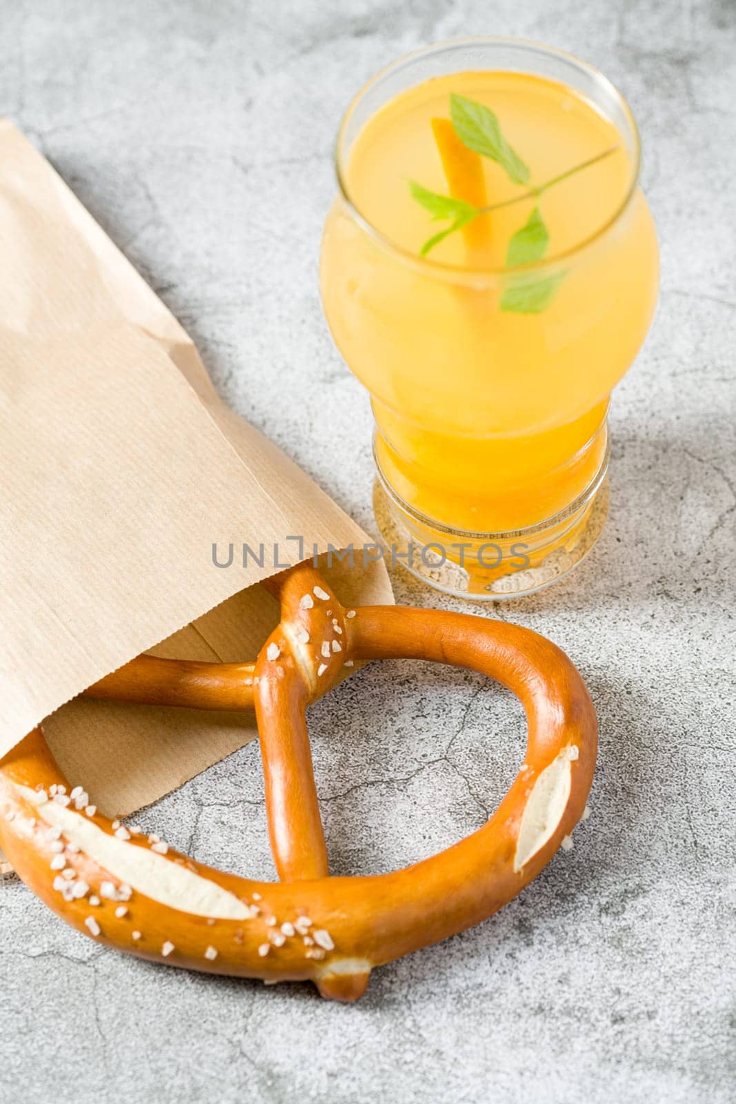 Pretzel wrapped in wrapping paper with drink next to it on stone table