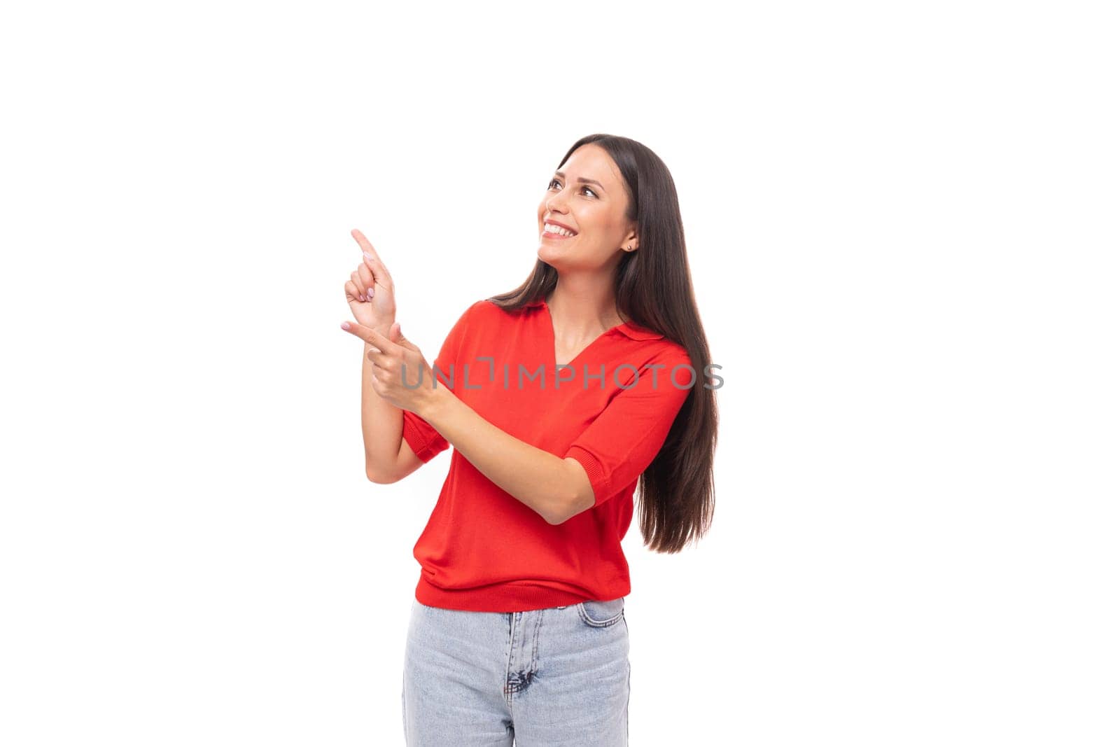 young european woman with black hair dressed in a red t-shirt shows empty space on the wall.