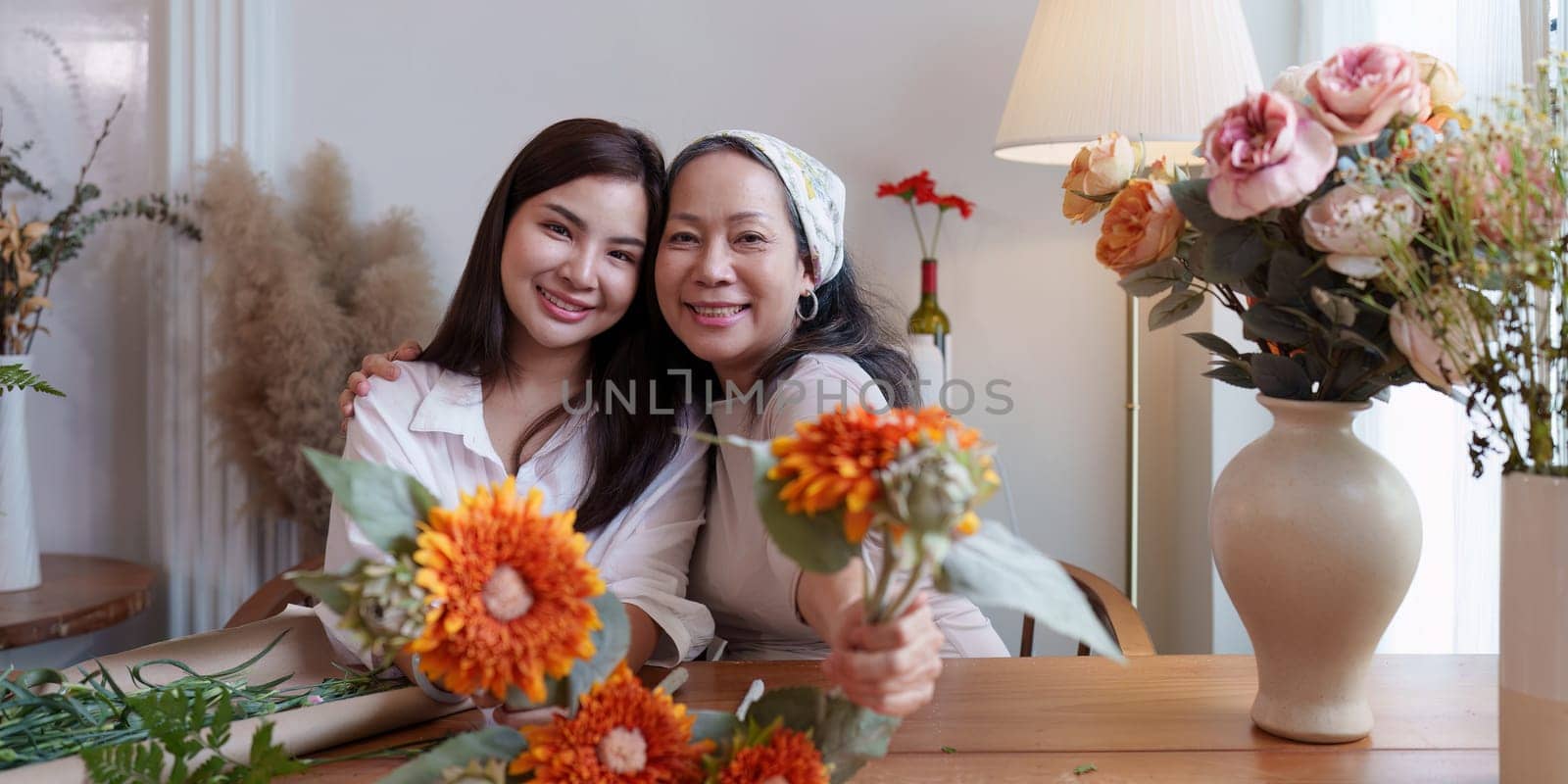 Startup, small business, flower shop. Young and older woman florist putting a flower on a vase.