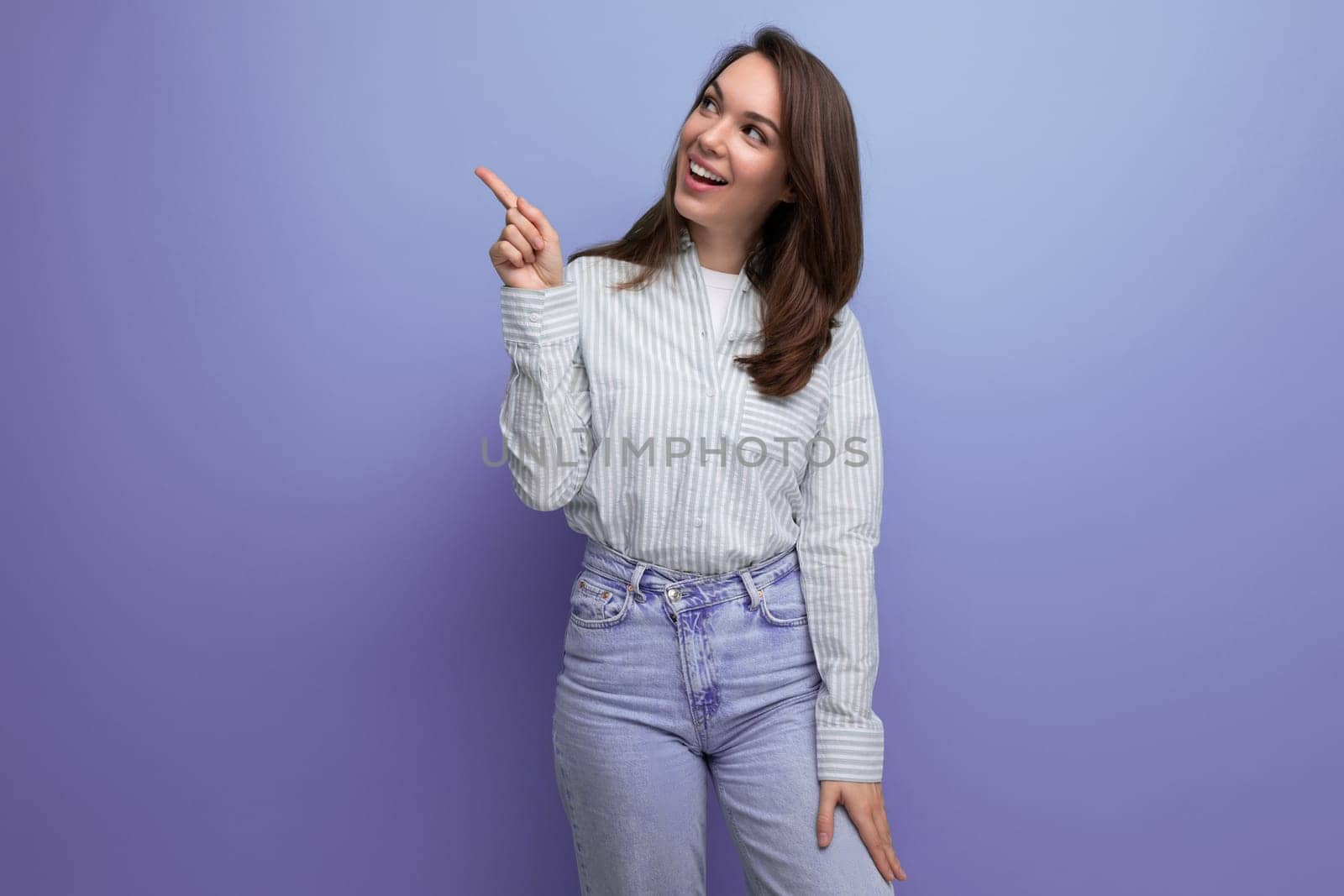 25 year old brown-haired female person dressed in a striped blouse points her index finger to the side.