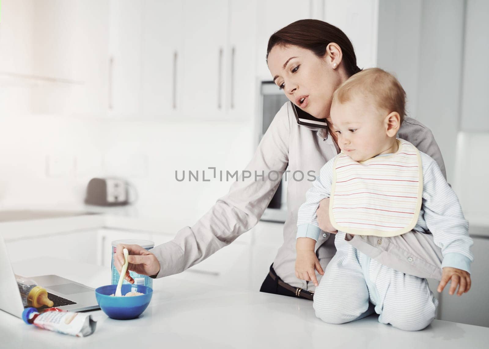 Family, baby and mother with multitasking, home and phone call with stress, feeding toddler and burnout. Mama, female parent and infant in the kitchen, smartphone and communication with frustration.