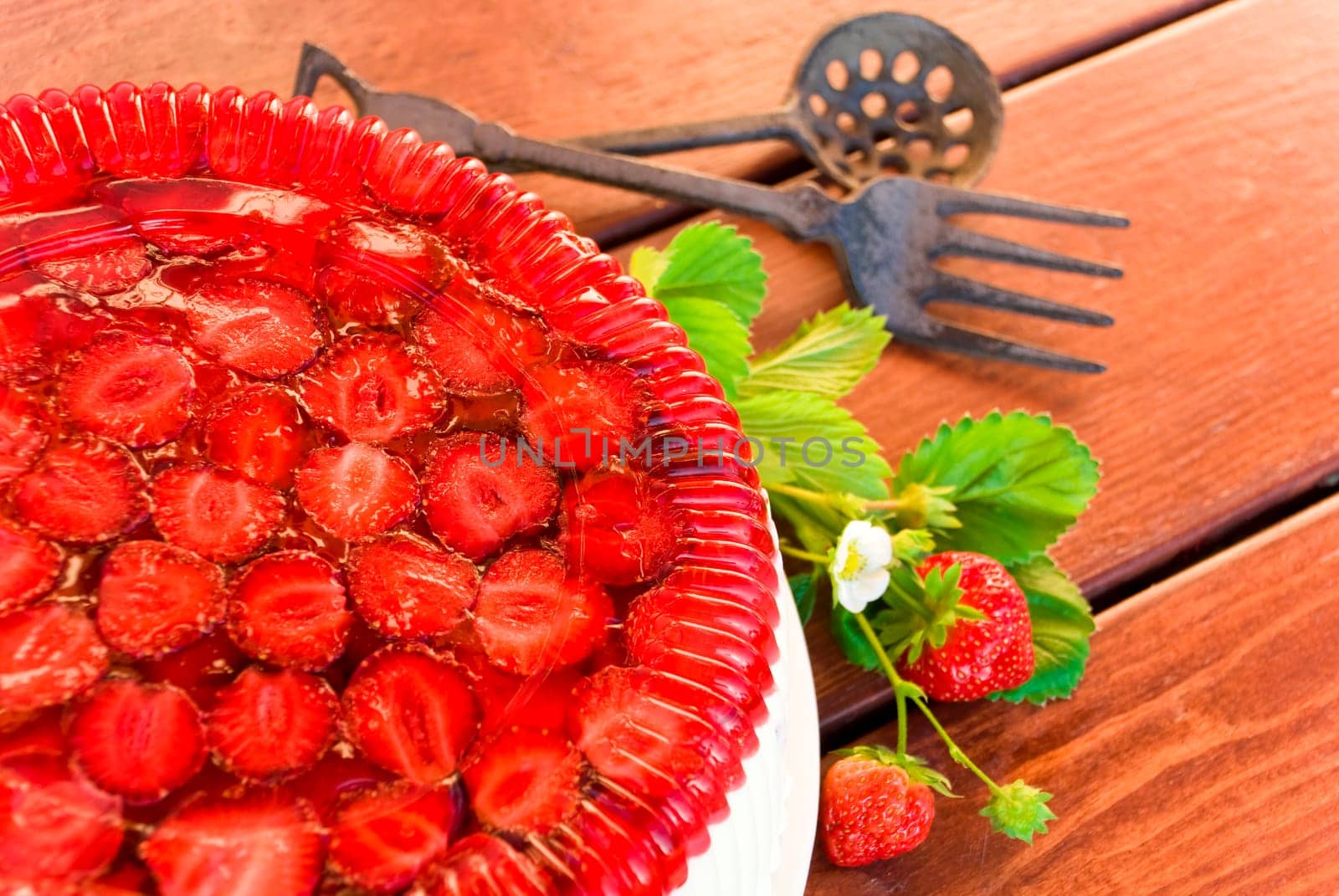 Cake with strawberries and whipped cream decorated with leaves on wooden background