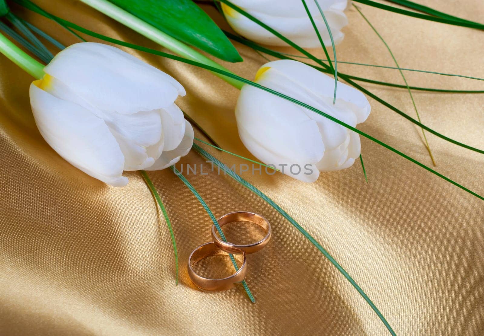 Two wedding rings on beautiful bright tulips, white flowers on silk background by aprilphoto