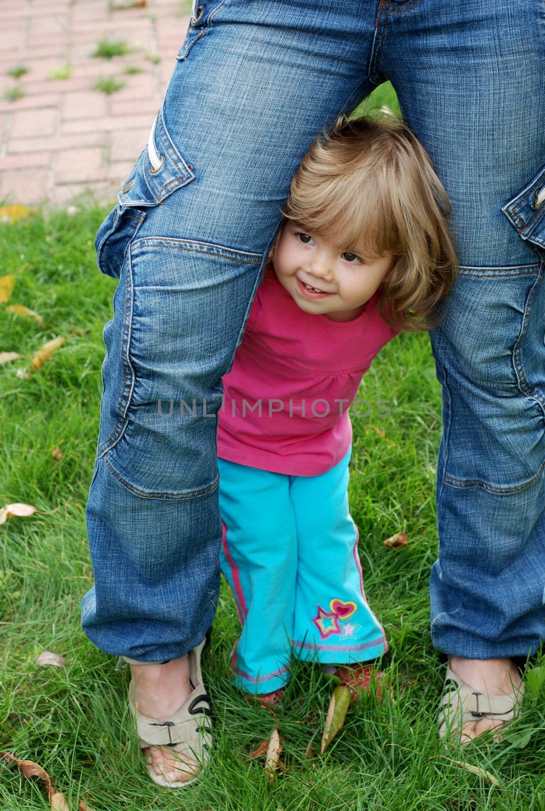 Childish shyness, timidity, insecurity. A defenseless child seeks support from a parent. Cute little girl hiding behind her mom by aprilphoto