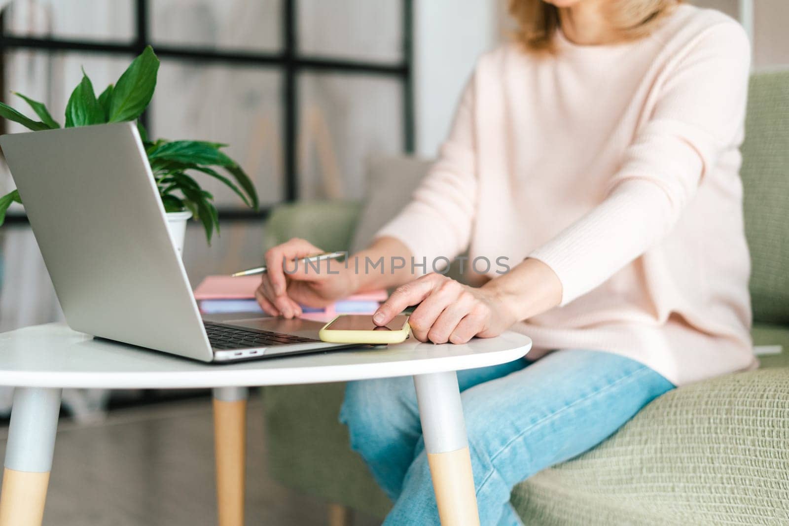 Cute adult senior mature woman in glasses checking text messages in her smartphone cell phone gadget, while doing online banking investment trading in her laptop computer by Ostanina