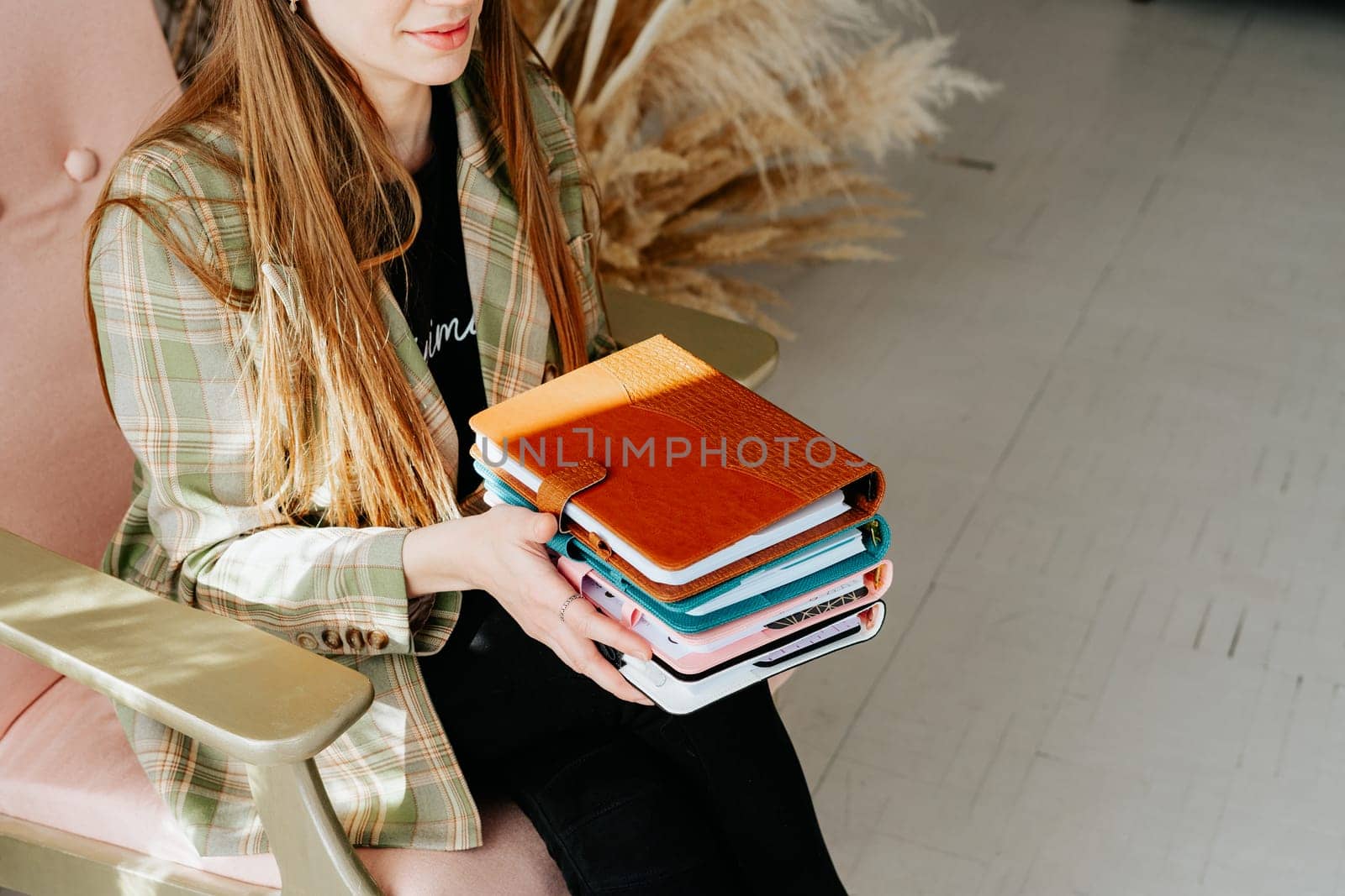 Business woman office secretary suit holding stack of notebooks. Student with a stack of notepads and dry flowers in the background. Cropped girl in a stylish office outfit holds books in her hands by Ostanina