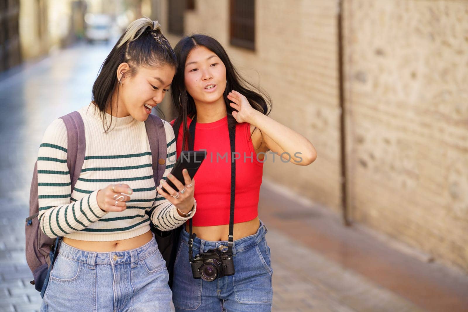 Young Asian women friends with backpacks and photo camera walking along street in Granada city while using map via mobile phone