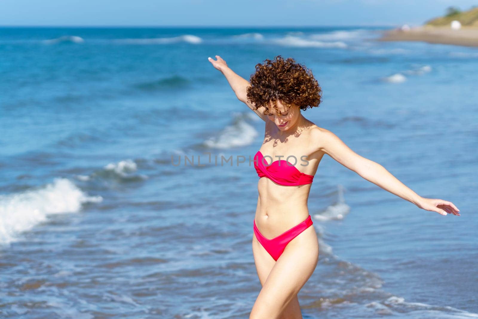 Joyful young lady in swimwear walking in sea with outstretched arms by javiindy