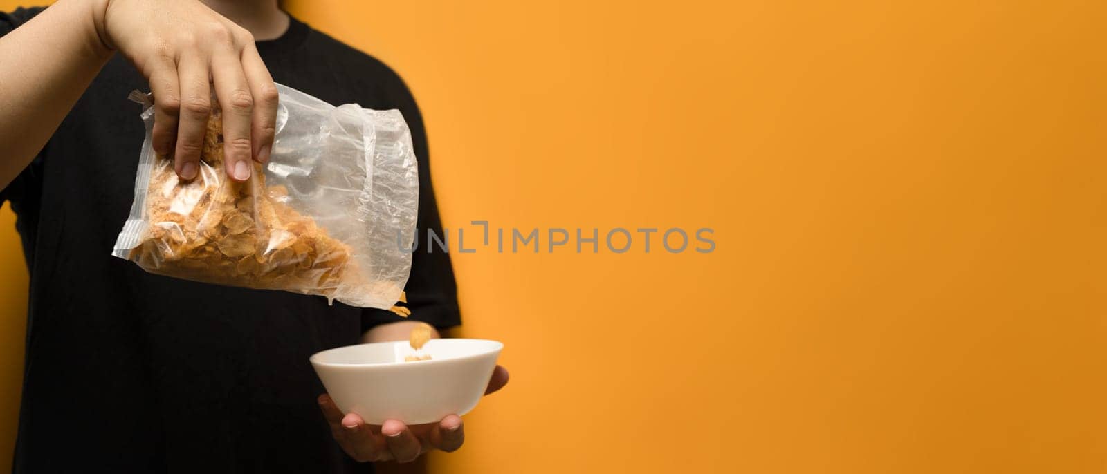 Cropped shot of man pouring cereals into a white bowl isolated on yellow background with space for advertising text message.