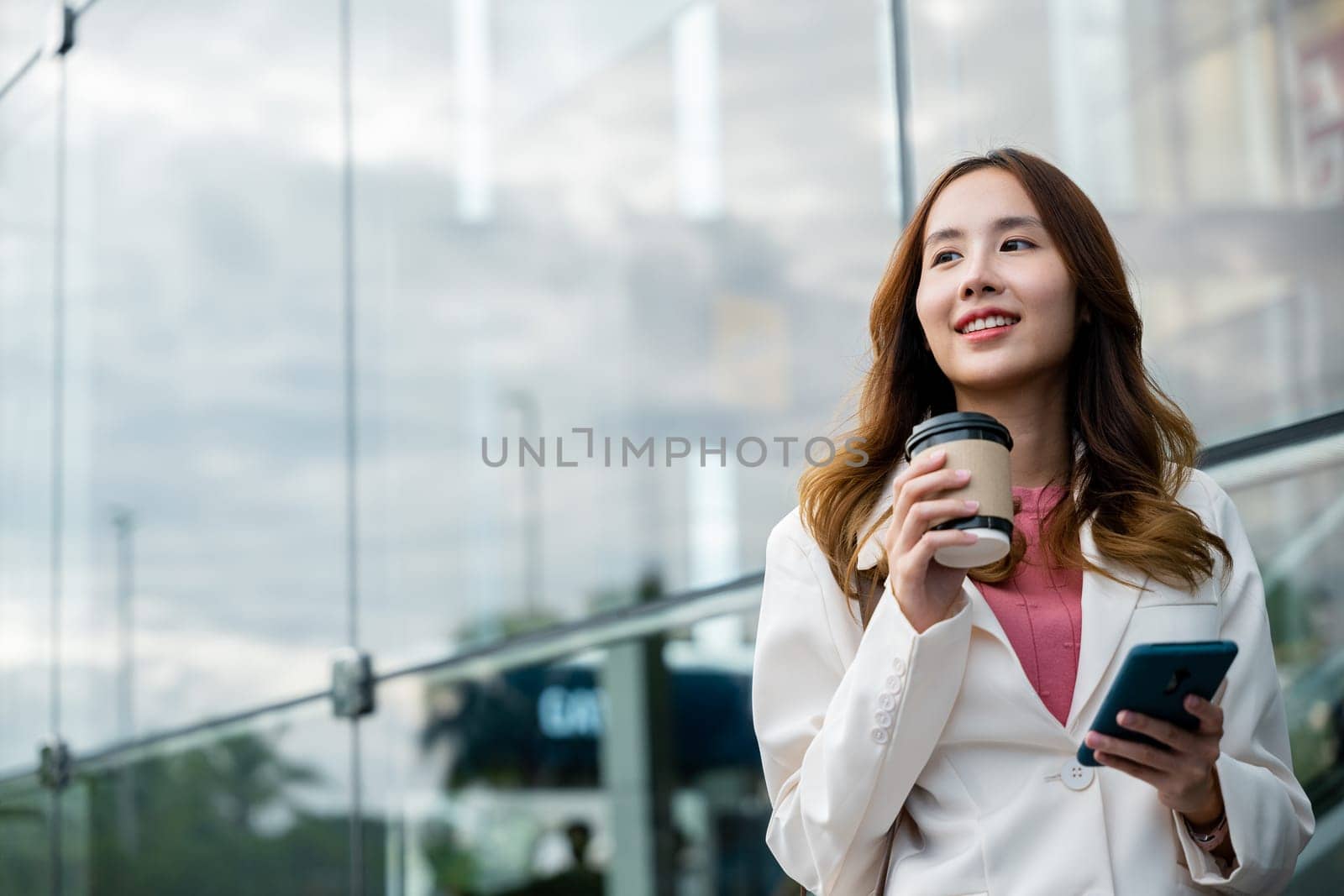 Asian businesswoman with smartphone and cup coffee standing street front building near office, Portrait woman smiling holding smart mobile phone with coffee take away going to work early in morning