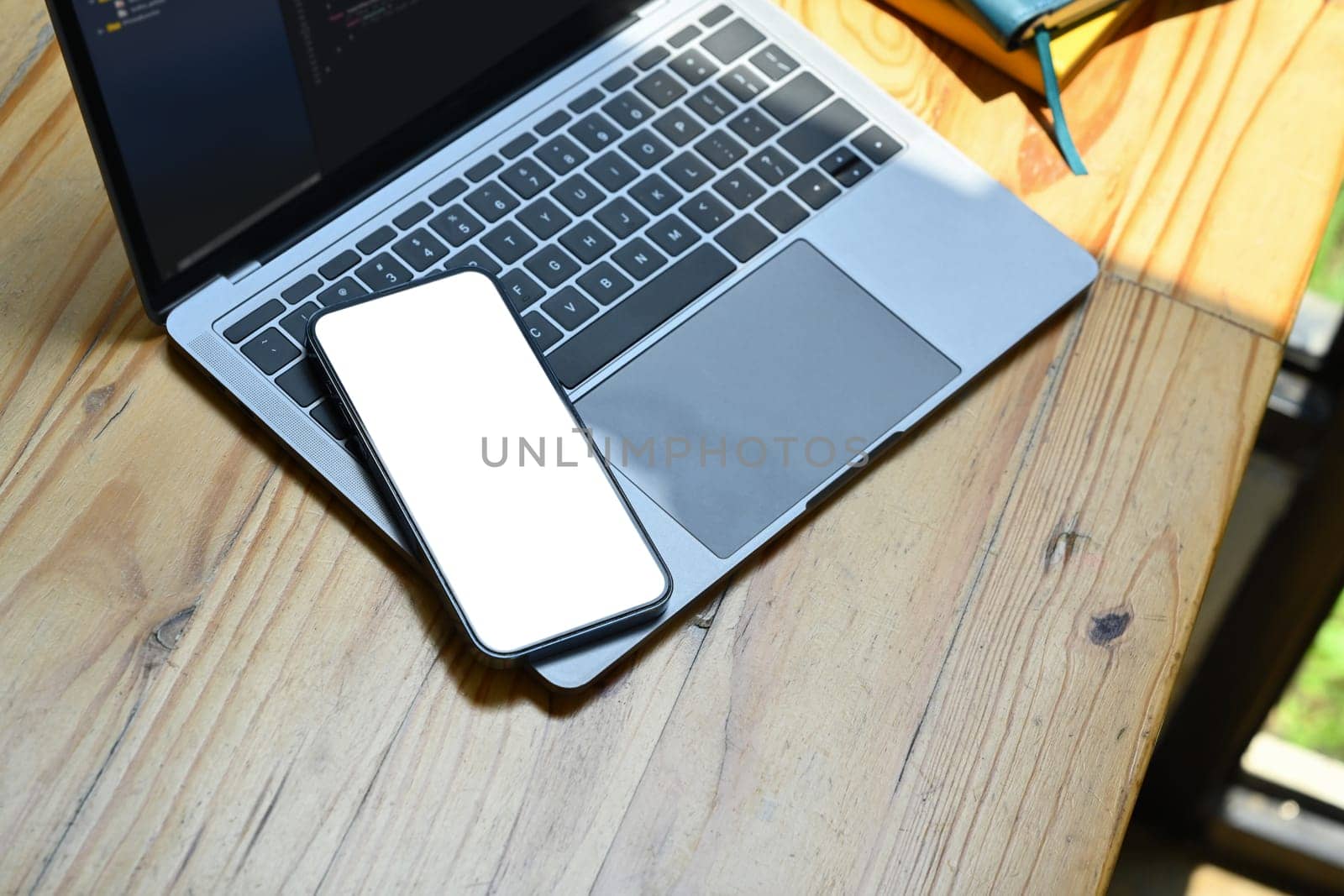 Smartphone with white blank screen and laptop computer on wooden office desk.