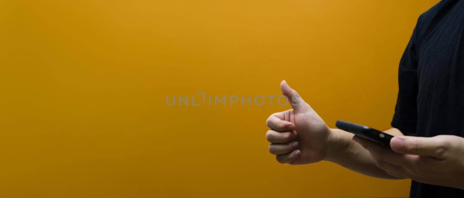 Man holding smartphone and showing thumb up isolated on yellow background with copy space for text.