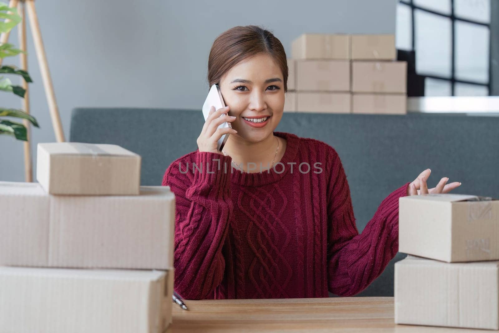 Cheerful small online business owner processing Internet store order for shipping, typing on laptop, speaking mobile phone, using gadgets for communication with clients by nateemee