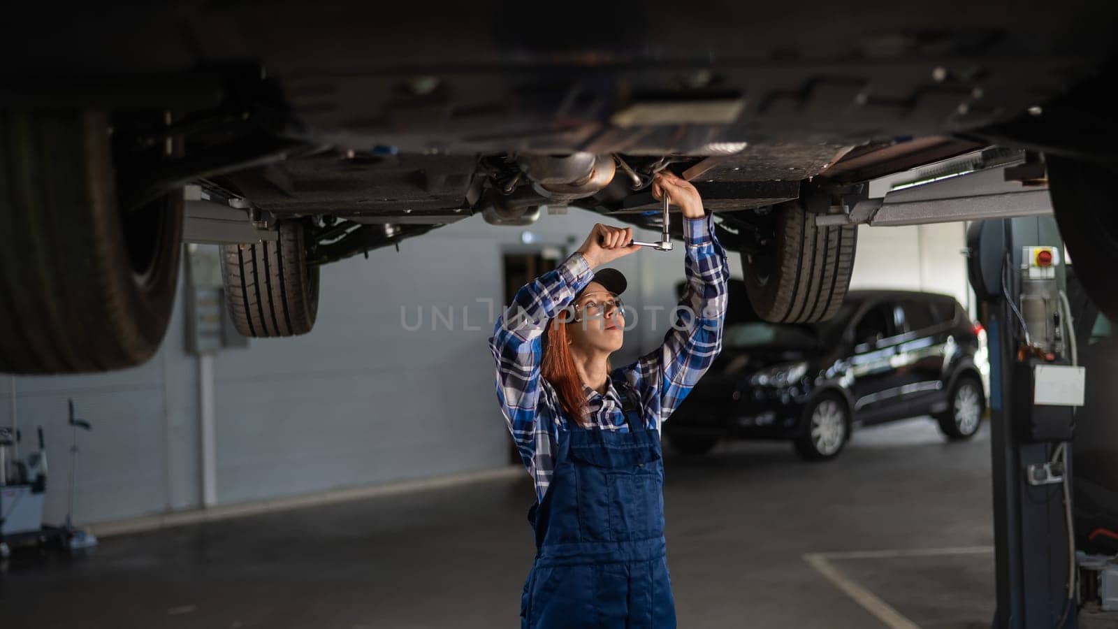 Female mechanic unscrew the nuts on the bottom of the car that is on the lift. A girl at a man's work. by mrwed54