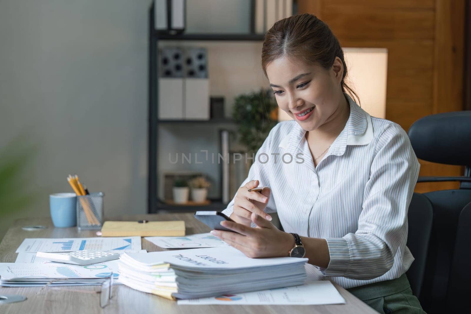 Smiling young business woman, happy beautiful professional lady worker holding smartphone using cellphone mobile working at office checking cell phone at workplace.