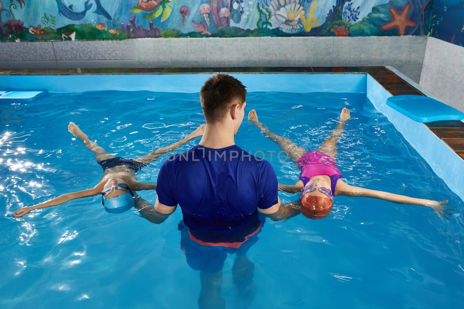 Little child learning to swim in pool with a teacher