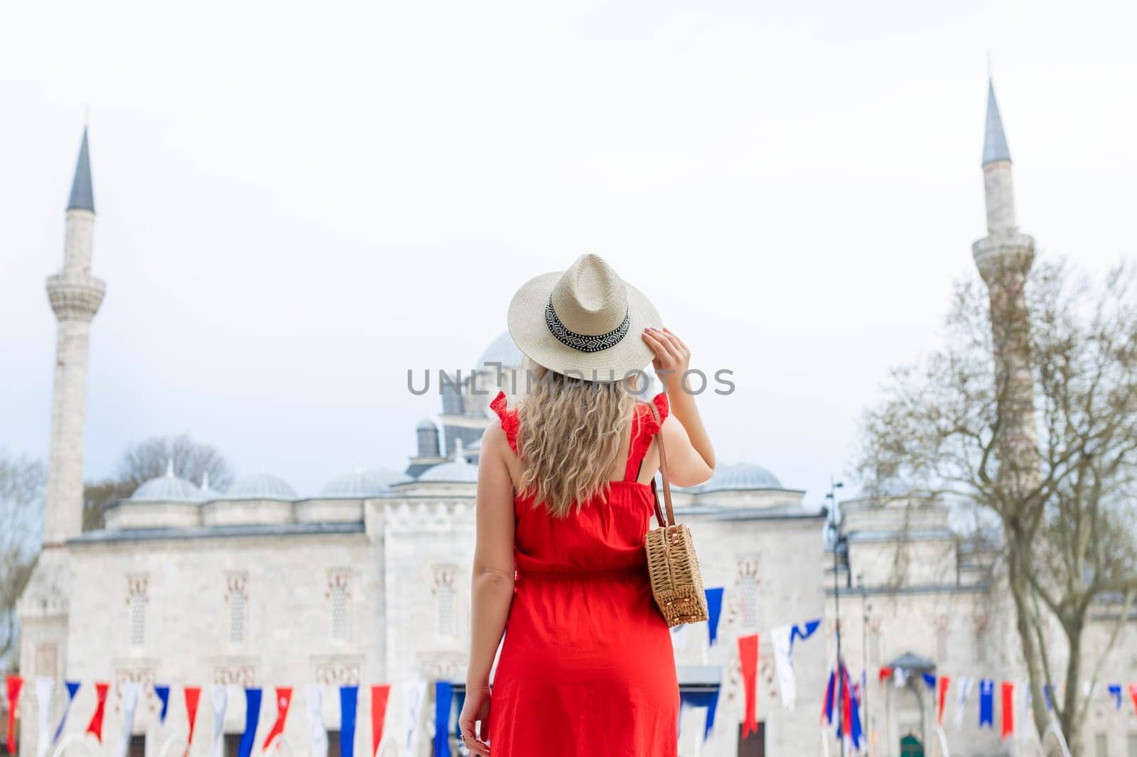 A beautiful travel blogger girl in a long red dress and a straw hat is photographed at the ancient sights in Istanbul in Turkey.