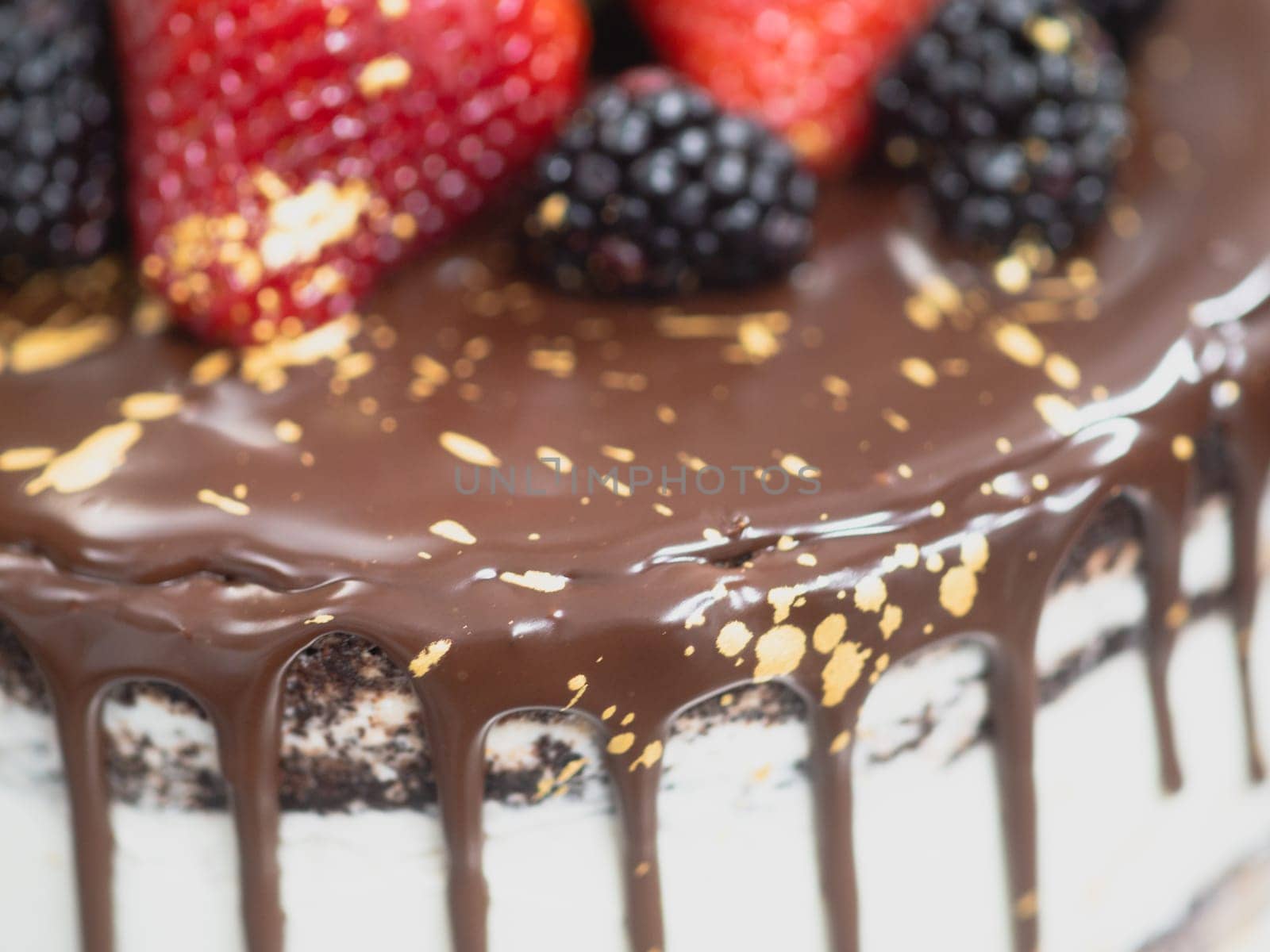 pastry chef preparing a chocolate frosted dripped icing cup cake with sweet fruit topping and golden brush strokes