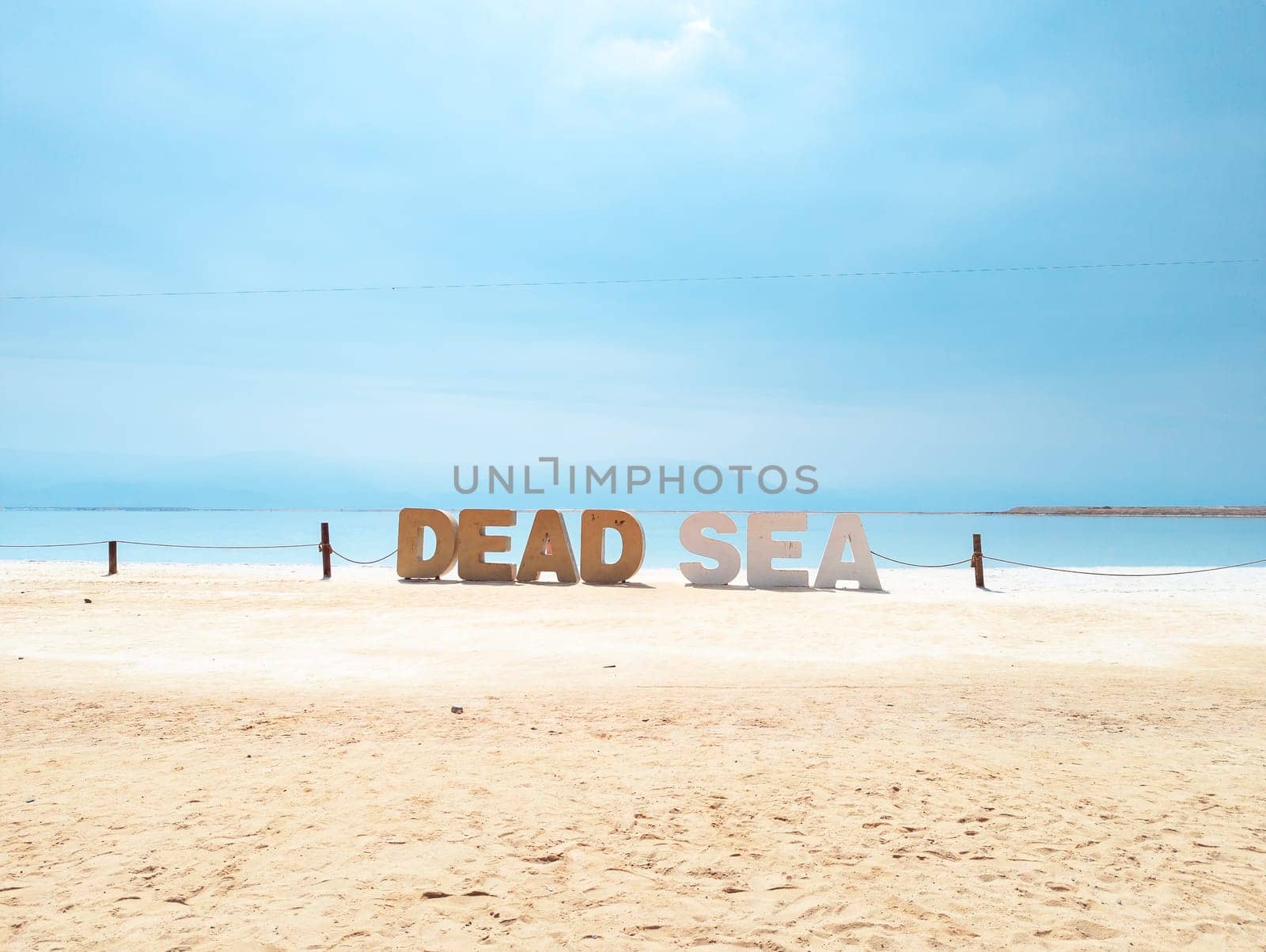 Landscape view on Dead Sea salt crystals formations, clear cyan green calm water with big letters saying Dead sea at Ein Bokek beach, Israel