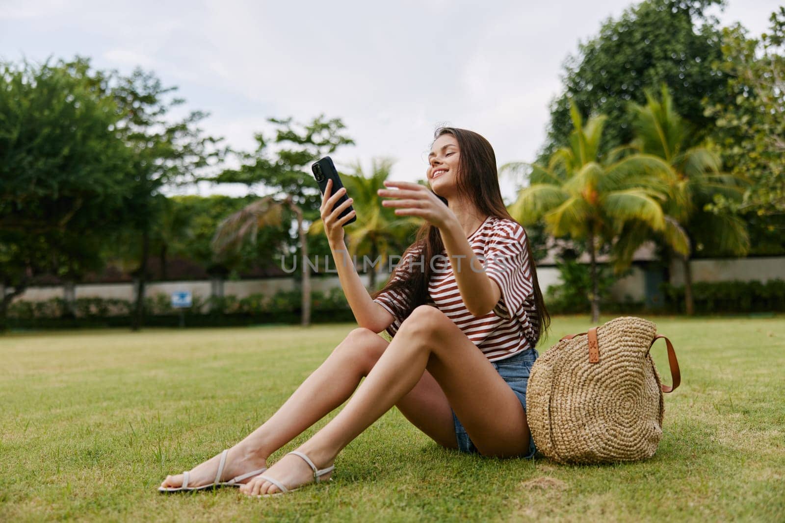 student woman t-shirt park palm nature blogger grass smartphone tree outside smiling lifestyle bag outdoor shirt happy cell caucasian summer striped phone