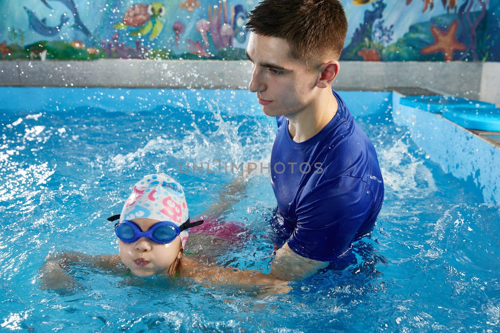 Little girl learning how to swim in pool with teacher by Mariakray