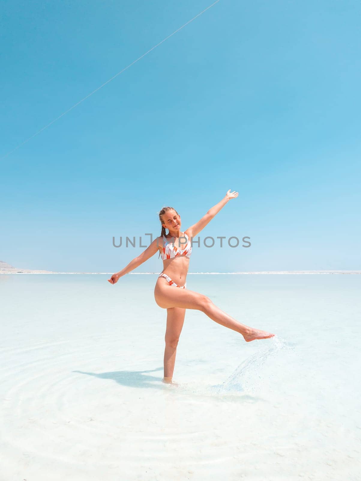 Beautigul girl in swimming suit on Dead sea salt crystals formation coastline, clear cyan green water at Ein Bokek beach, Israel. Dead sea resort holiday