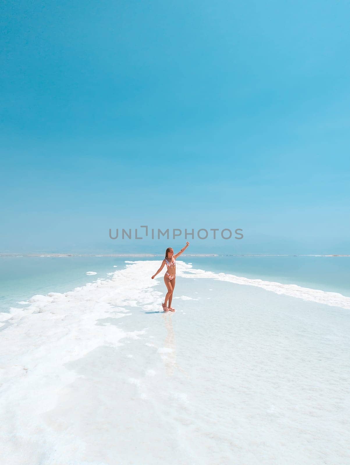 Beautigul girl in swimming suit on Dead sea salt crystals formation coastline, clear cyan green water at Ein Bokek beach, Israel by Len44ik