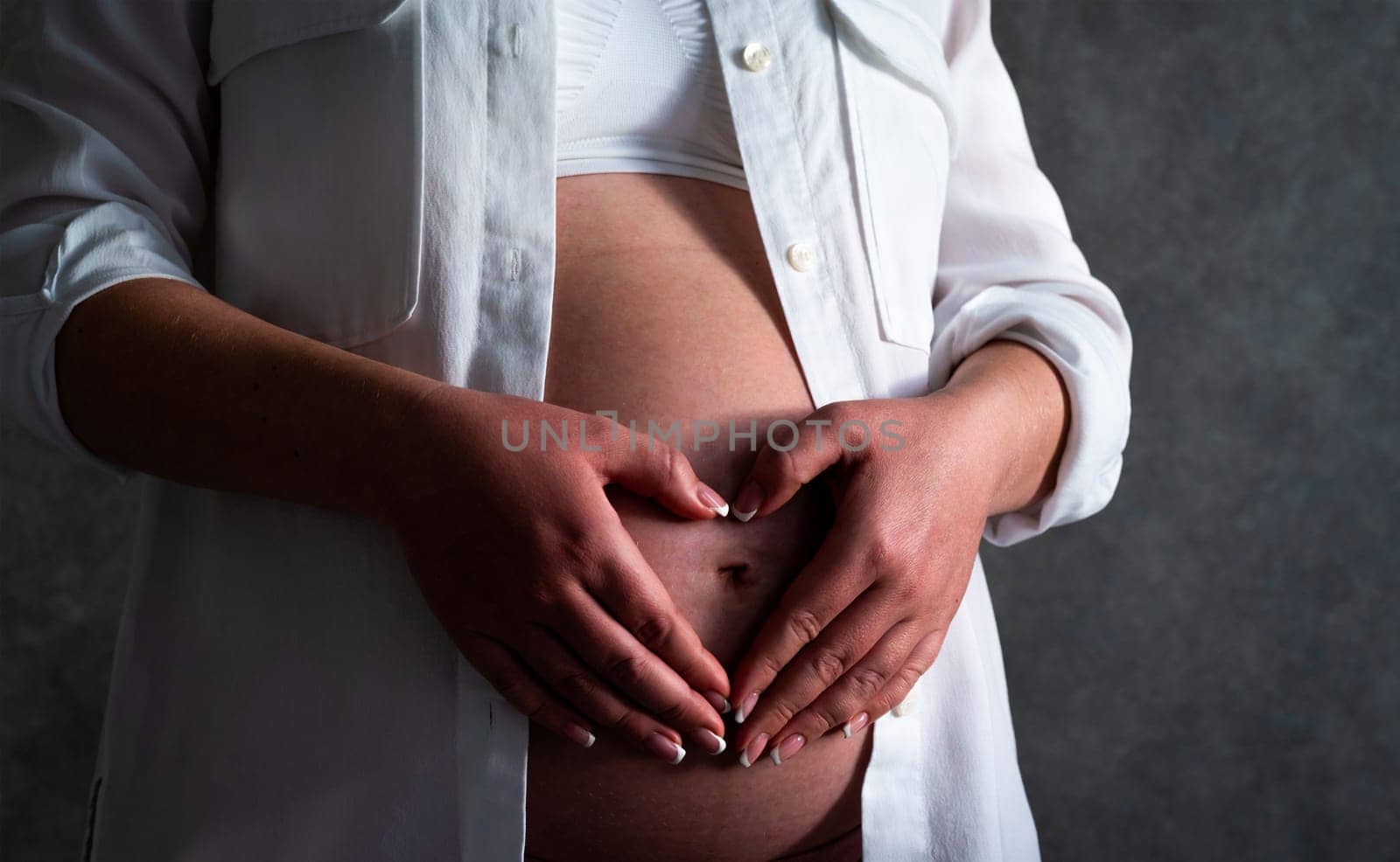 Belly of a pregnant woman. Pregnancy concept. Woman holding hands in heart shape by Mariakray