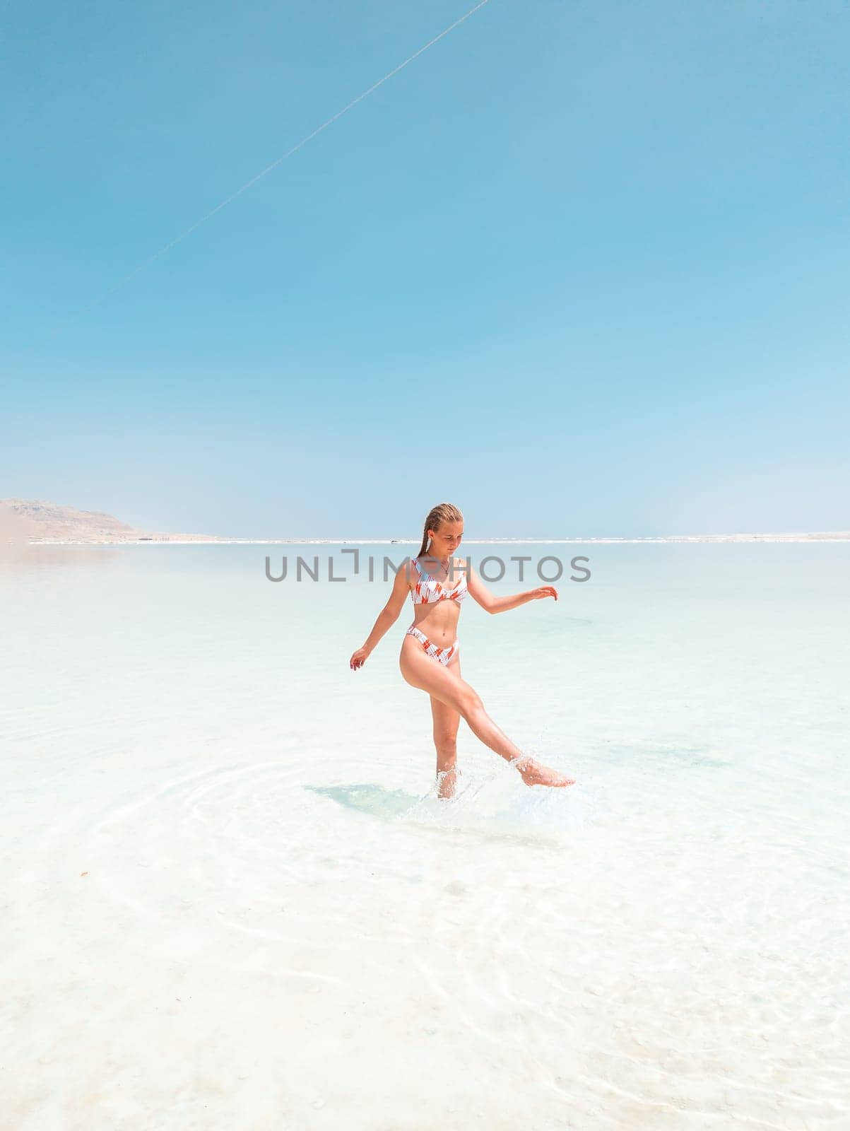 Beautigul girl in swimming suit on Dead sea salt crystals formation coastline, clear cyan green water at Ein Bokek beach, Israel. Dead sea resort holiday