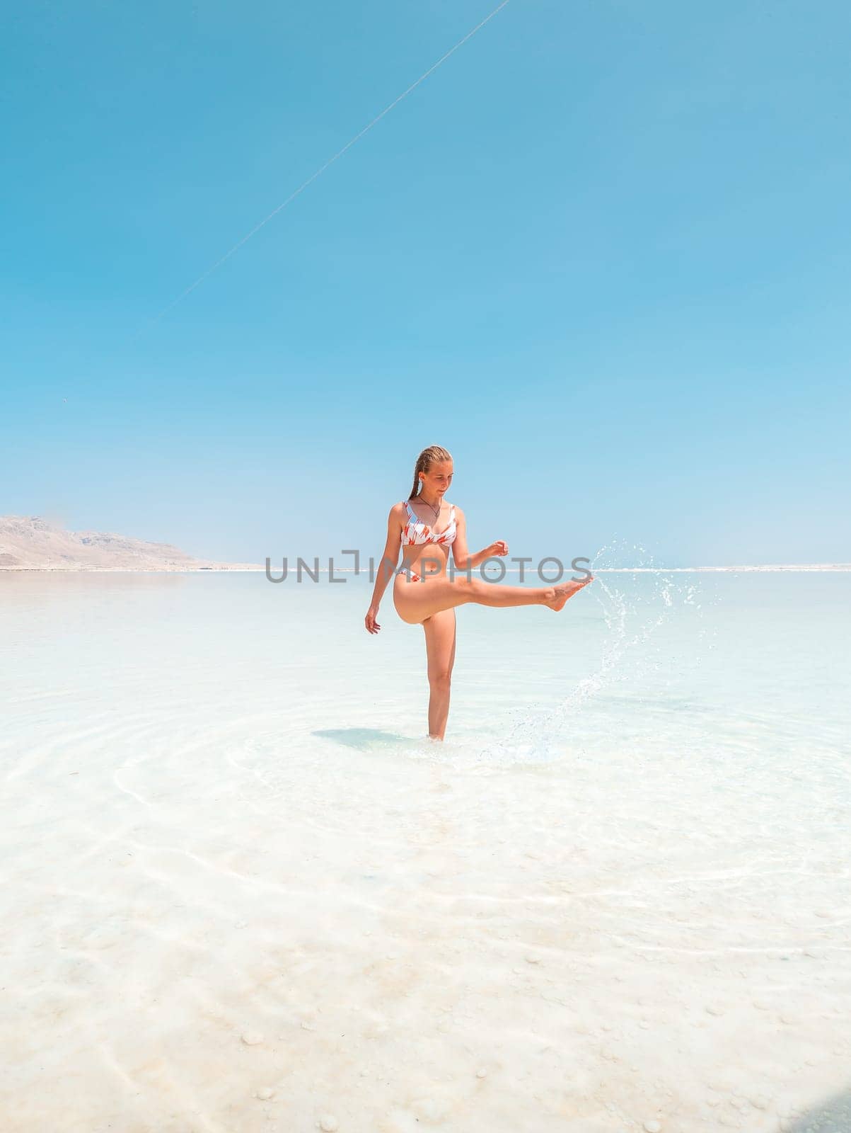 Beautigul girl in swimming suit on Dead sea salt crystals formation coastline, clear cyan green water at Ein Bokek beach, Israel by Len44ik