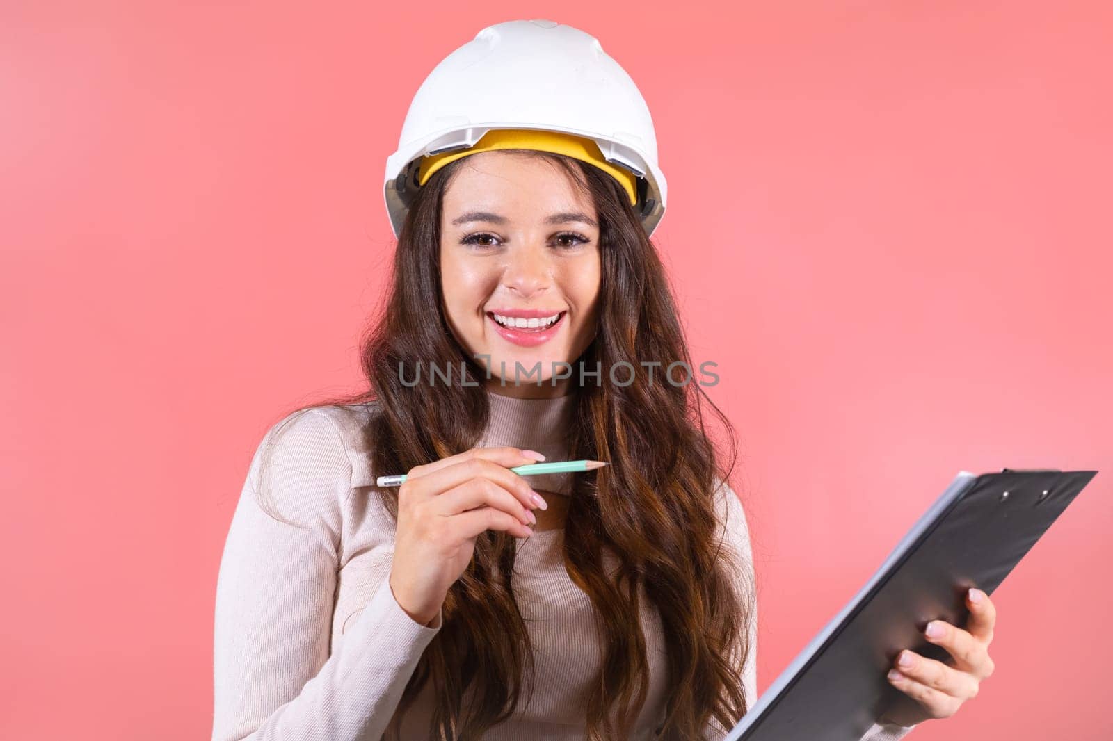 A happy brunette architect in a helmet checks the list on the pink background.