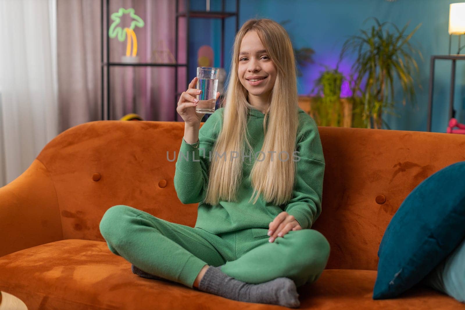 Thirsty woman holding glass of natural aqua make sips drinking still water preventing dehydration sits at home living room. Caucasian girl with good life habits, healthy slimming, weight loss concept