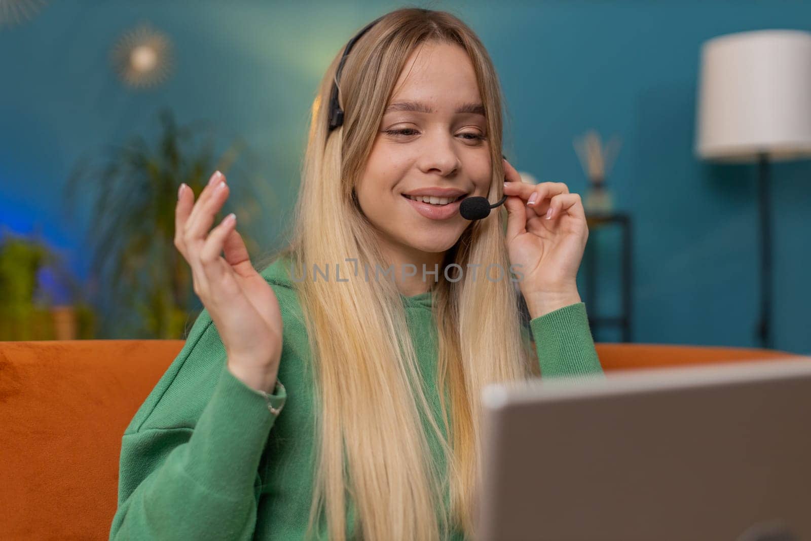 Caucasian woman wearing headset, freelance worker, call center or support service operator helpline, having talk with client or colleague communication support waving hello. Girl at home room on sofa