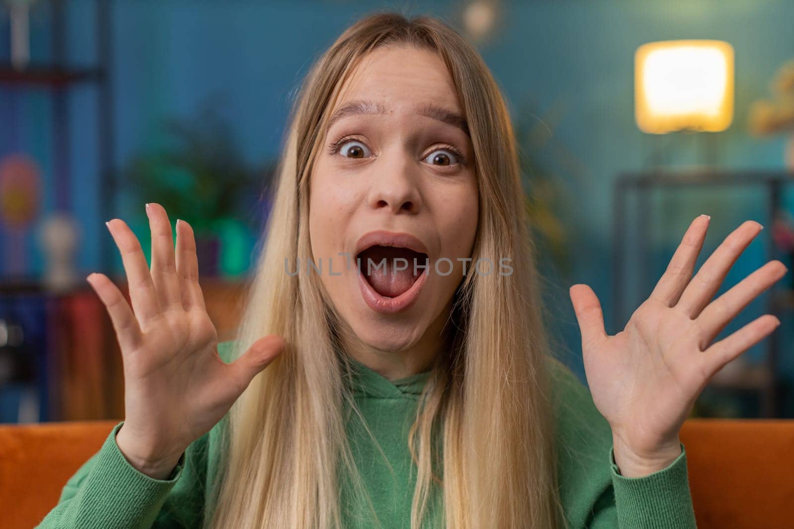 Oh my God, Wow. Excited amazed young woman surprised looking at camera with big eyes, shocked by sudden victory, good win news, celebrating. Portrait of Caucasian girl at home apartment room on sofa
