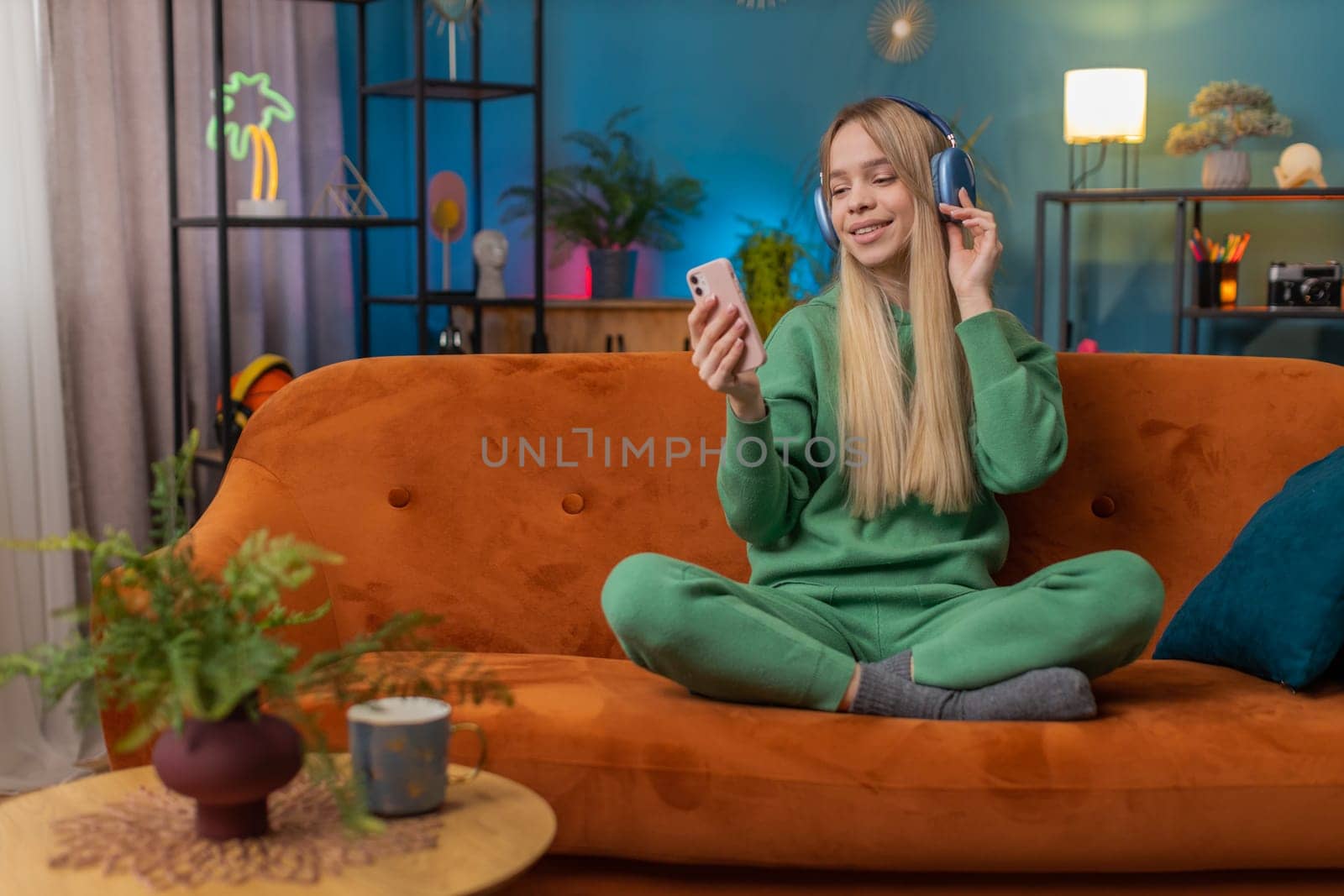 Happy overjoyed Caucasian woman in wireless headphones relaxing sitting on couch at home apartment choosing listening favorite energetic disco dancing music. People weekend daytime leisure activities