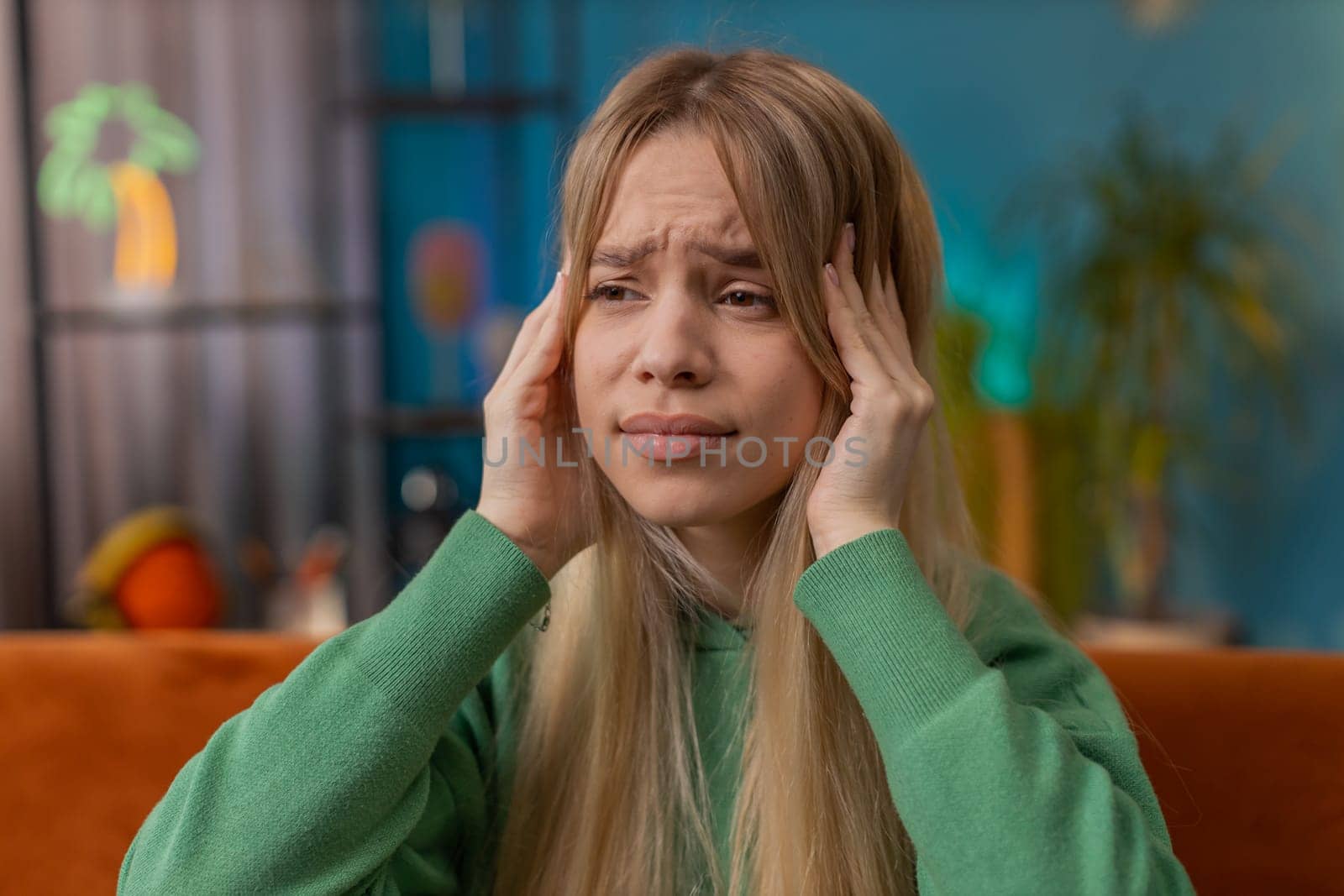 Displeased woman rubbing temples to cure headache problem, suffering from tension and migraine stress grimacing in pain high blood pressure at home room apartment. Teen child girl on couch. Lifestyles