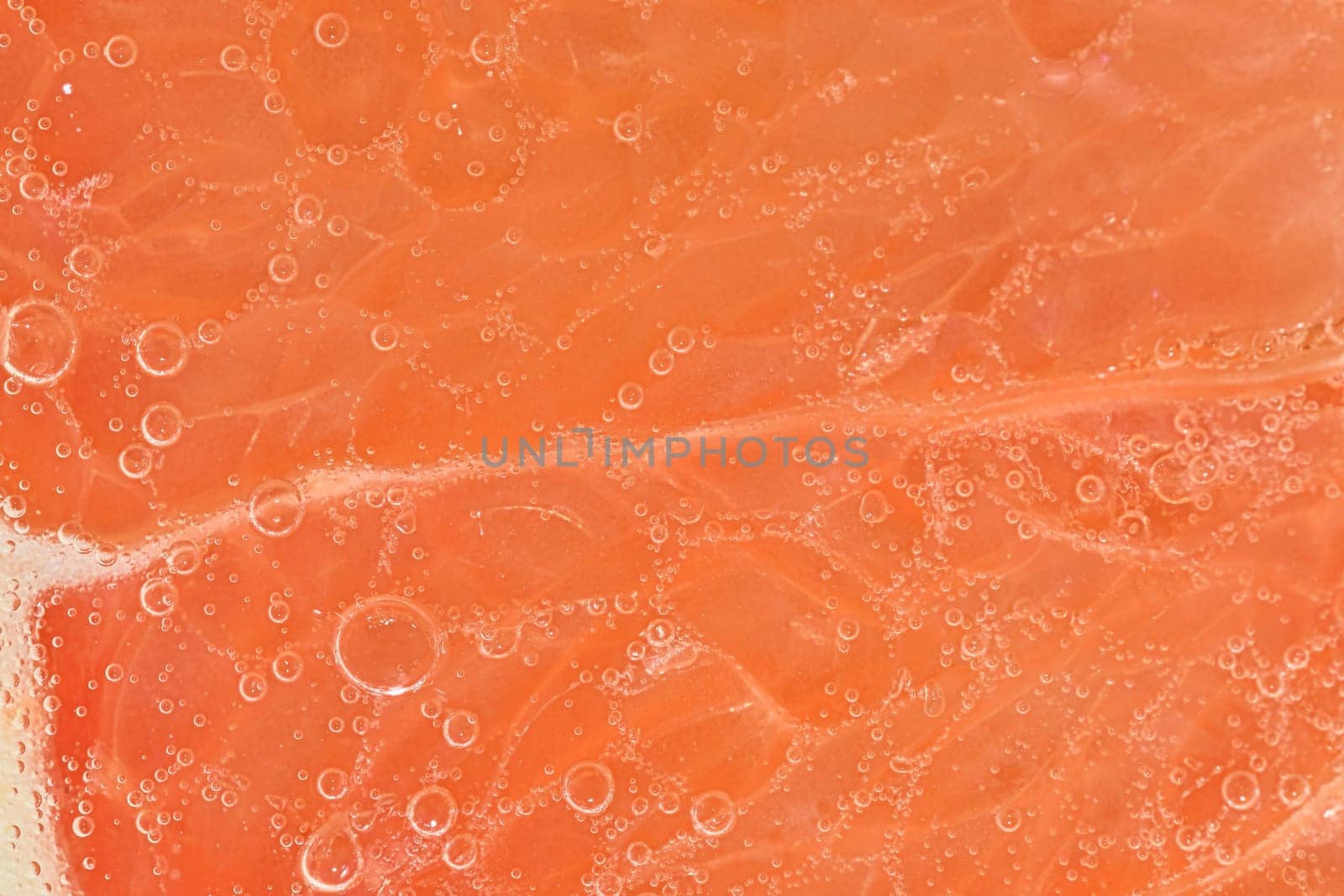 Close-up of a grapefruit slice in liquid with bubbles. Slice of ripe grapefruit in water. Close-up of fresh grapefruit slice covered by bubbles. Macro horizontal image