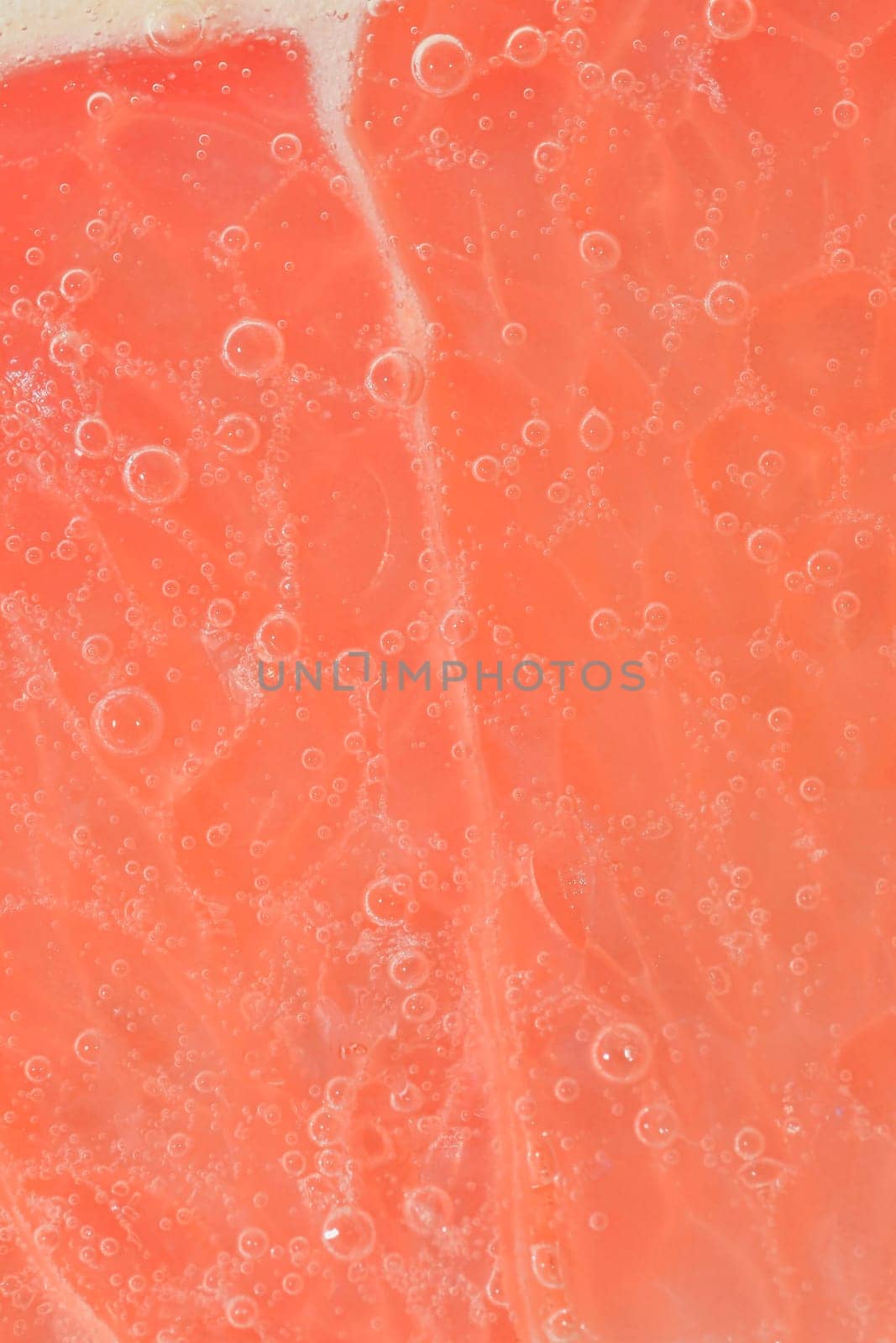 Close-up of a grapefruit slice in liquid with bubbles. Slice of ripe grapefruit in water. Close-up of fresh grapefruit slice covered by bubbles. Macro vertical image. Abstract and background