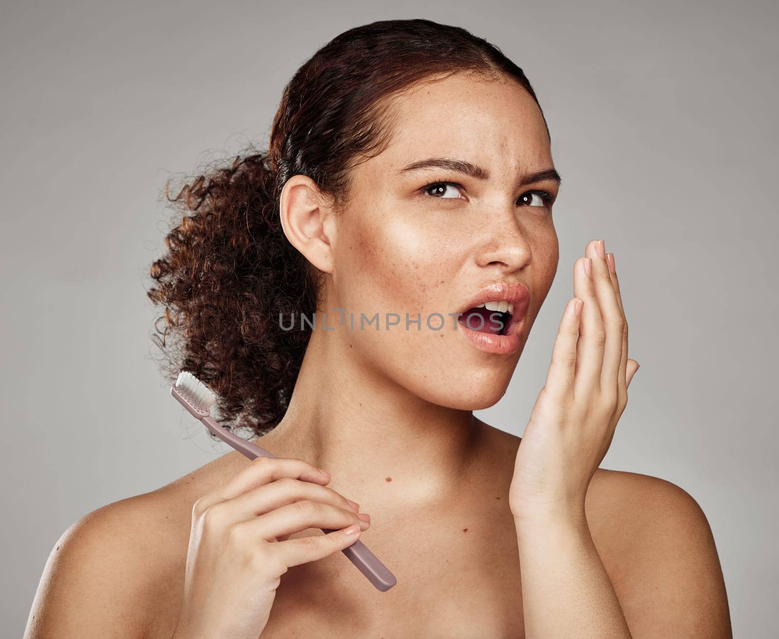 Woman, bad breath and smelling mouth for dental problem, odor and poor oral health in hand. Female with toothbrush for brushing teeth and self care for halitosis, cavity or decay on grey background by YuriArcurs